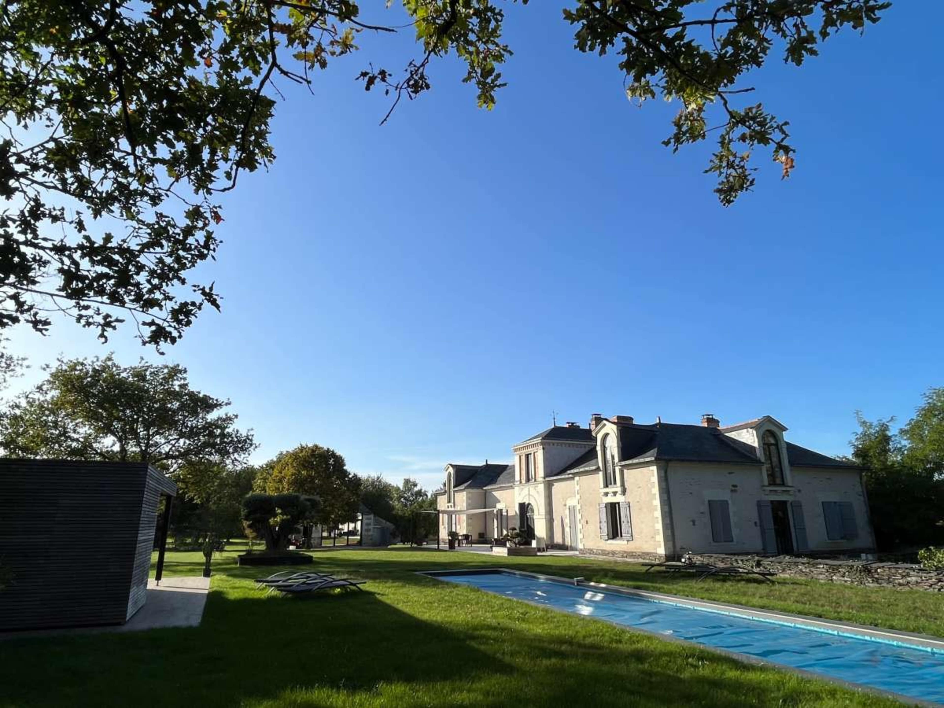 A large, modern house with a swimming pool is surrounded by a well-maintained lawn and trees under a clear blue sky.