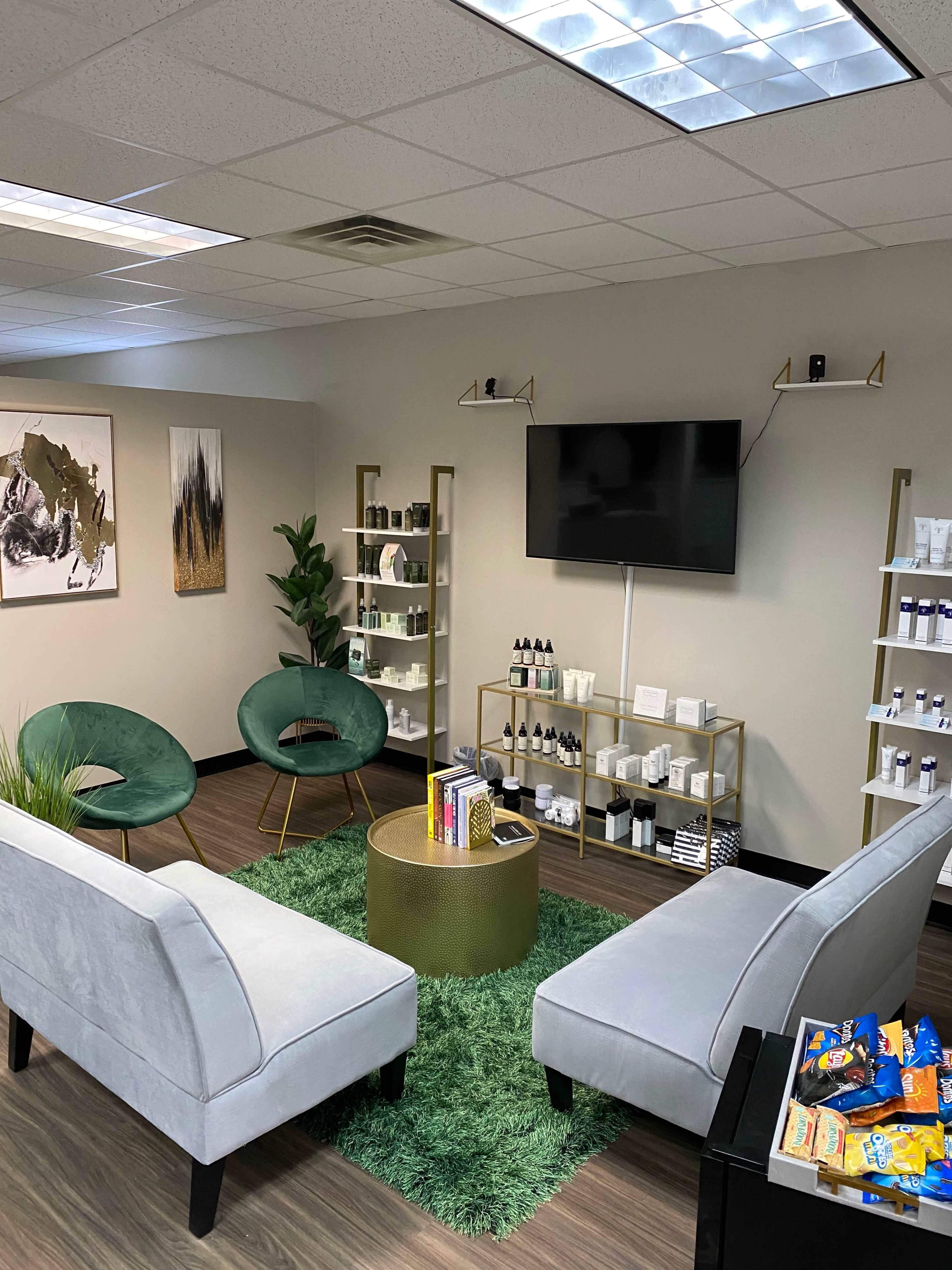 A modern waiting area with two green chairs, a coffee table, and shelves displaying various skincare products.