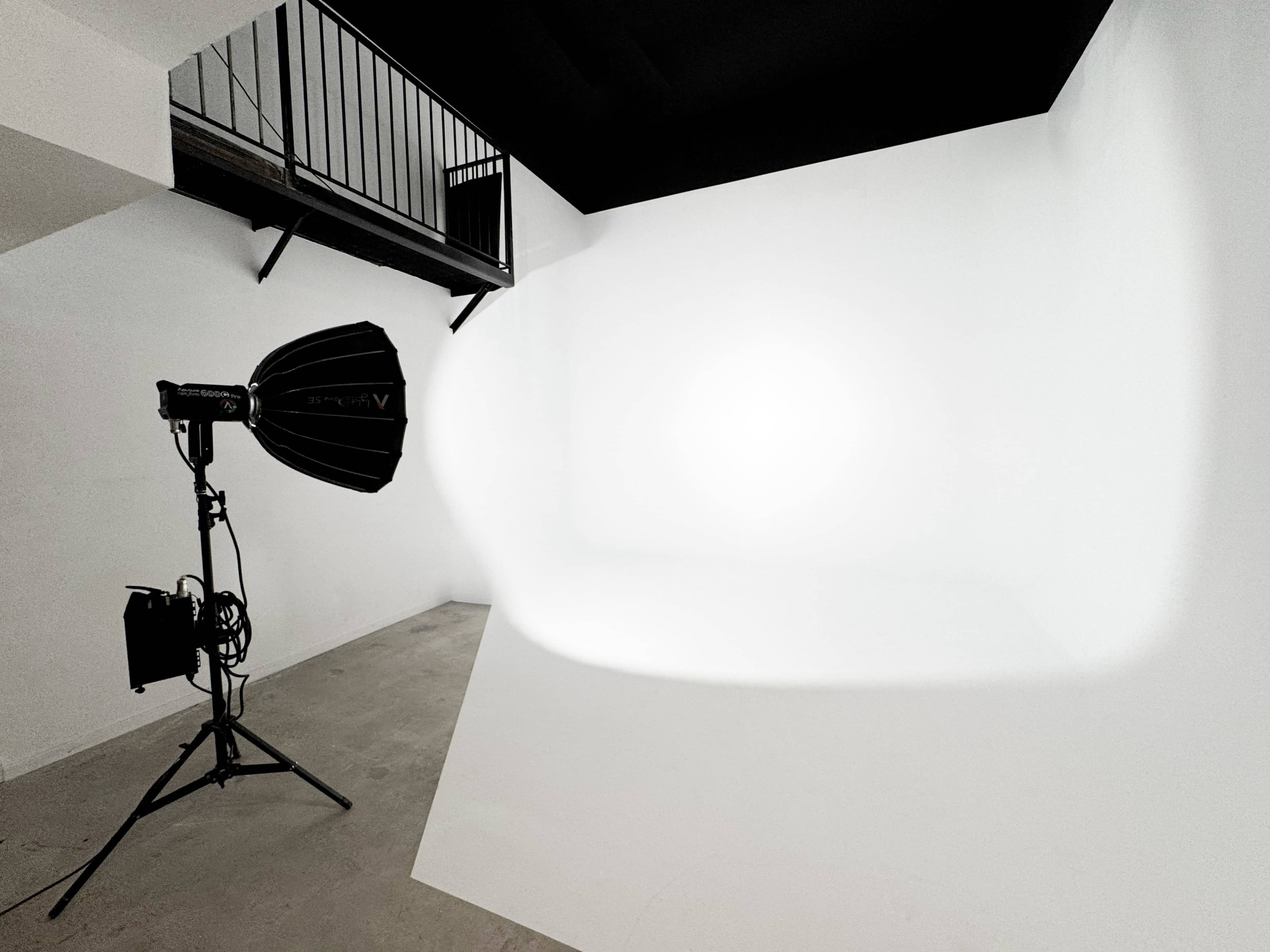 The image shows a photography studio with a spotlight positioned on a white backdrop and a staircase in the background.