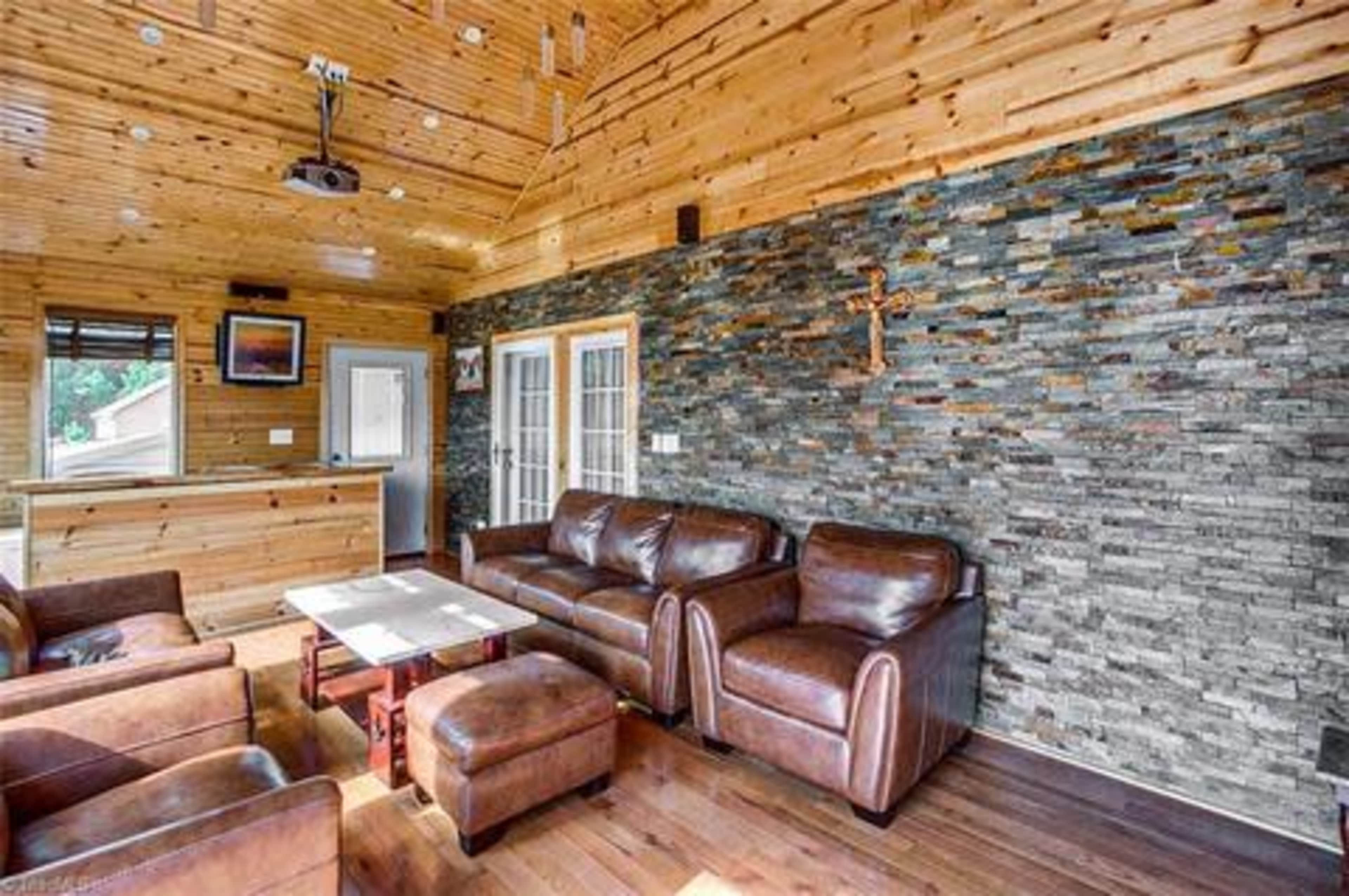 A seating area features brown leather sofas and a wooden table against a stone accent wall in a room with wooden paneling.