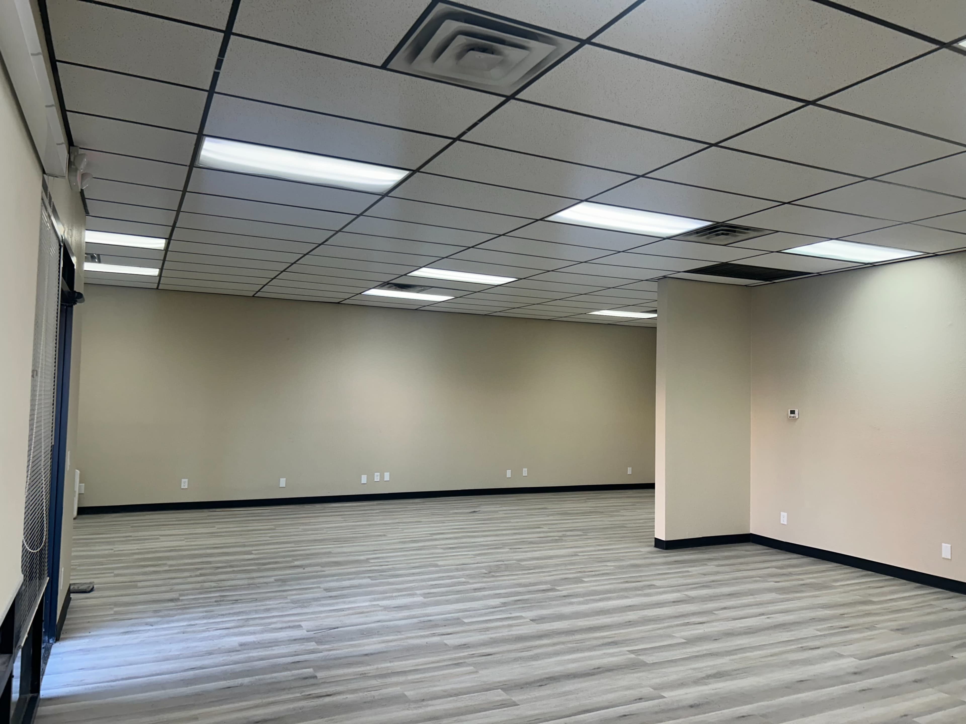 The image shows an empty commercial space with gray flooring, beige walls, and fluorescent ceiling lights.