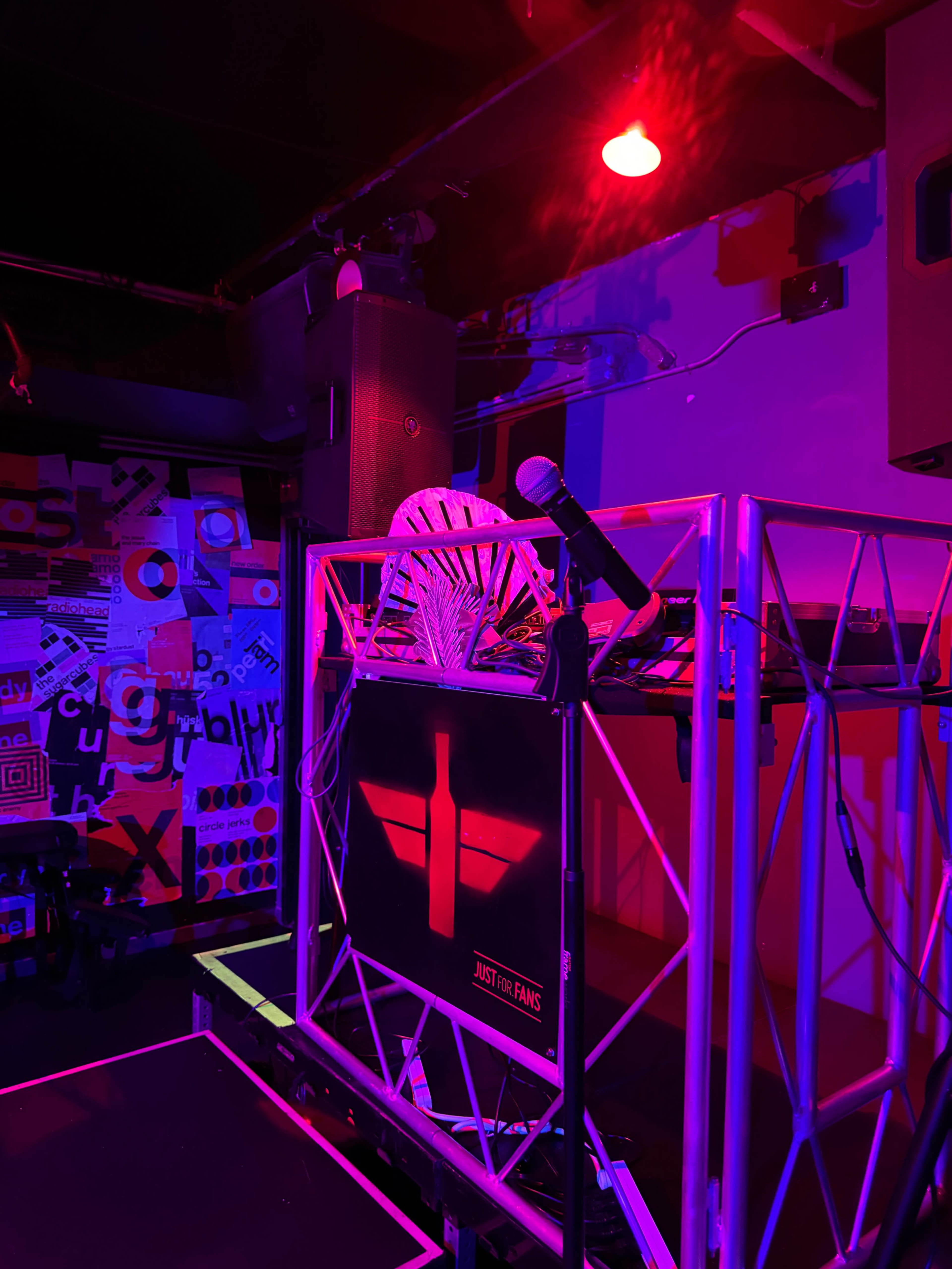 A DJ booth with a microphone and a chair, illuminated by red and purple lights in a colorful, abstract-themed venue.