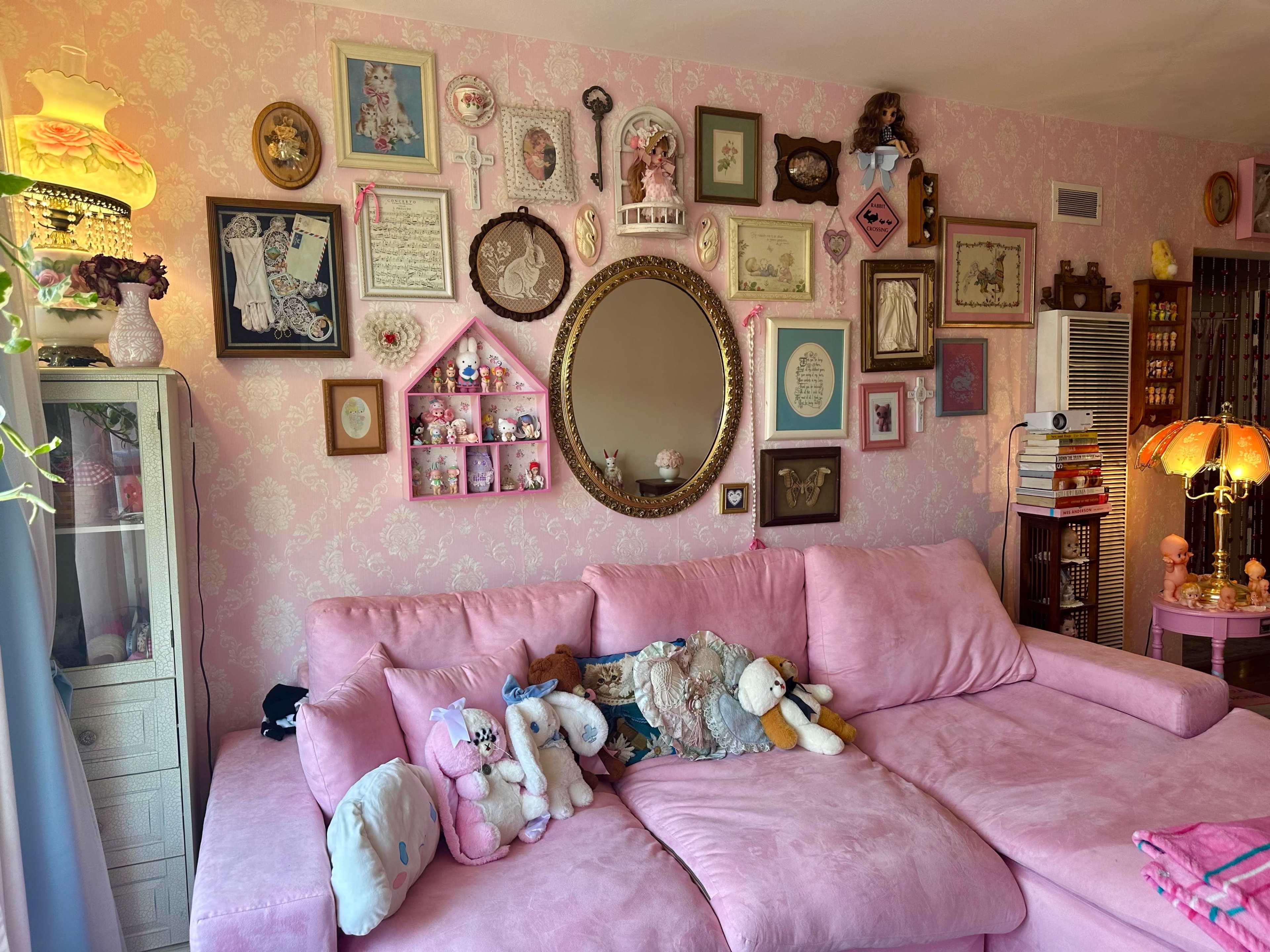 A pink sectional sofa adorned with plush toys, set against a wall decorated with various framed artworks and vintage decor.