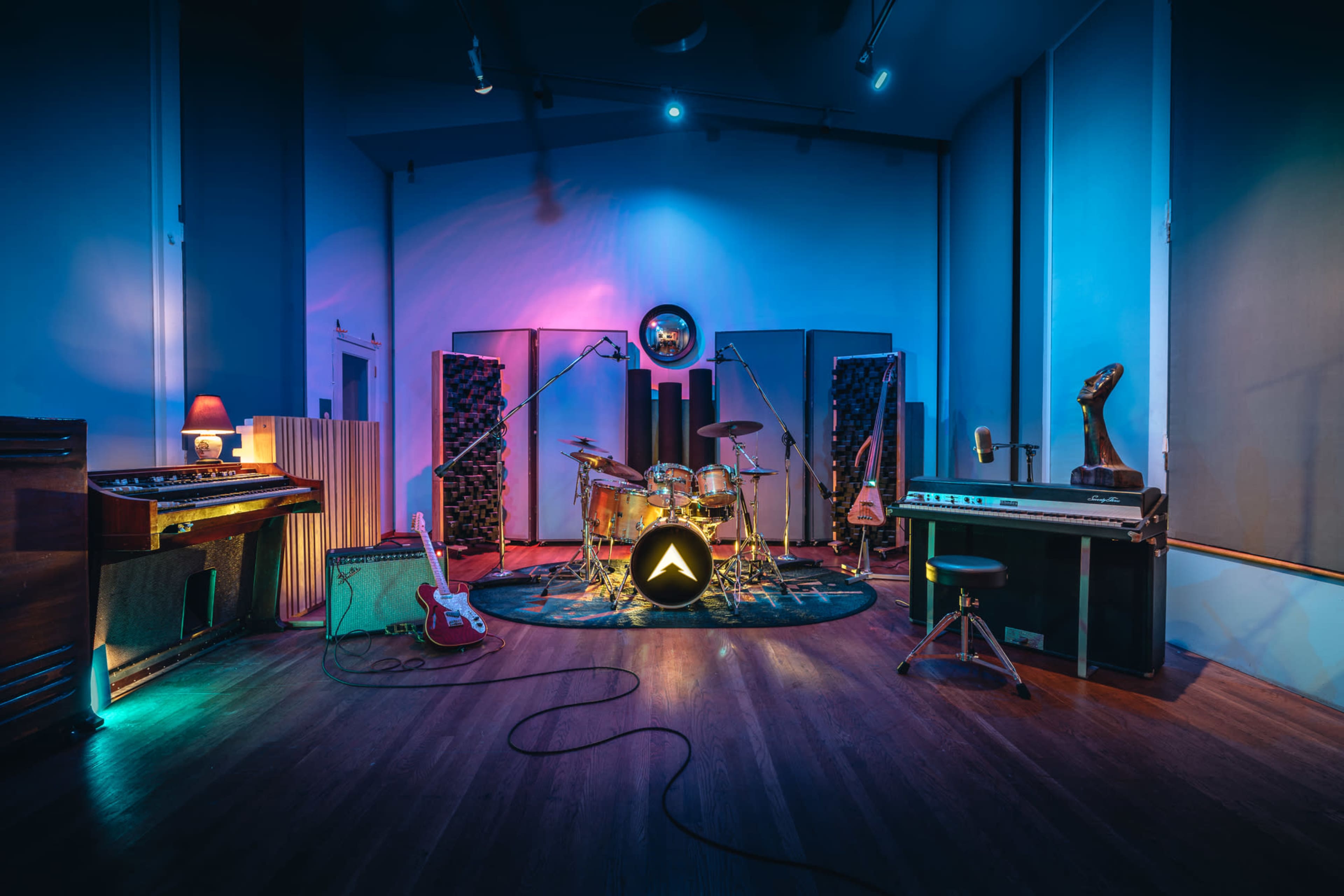 A music studio features a drum set, various instruments, and colorful lighting against a backdrop of soundproofing panels.
