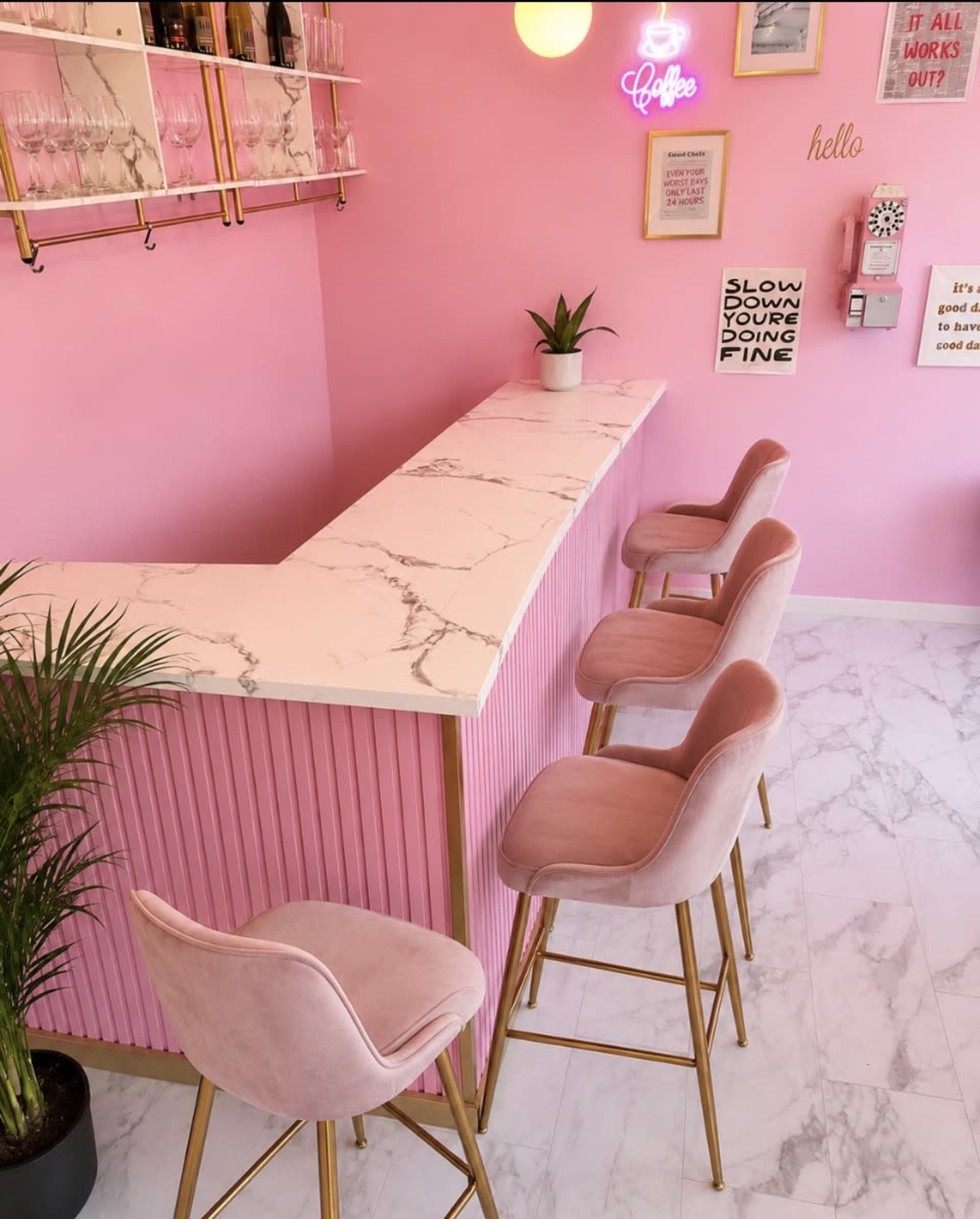 The image shows a brightly colored pink coffee bar with a marble countertop and four pink velvet stools.