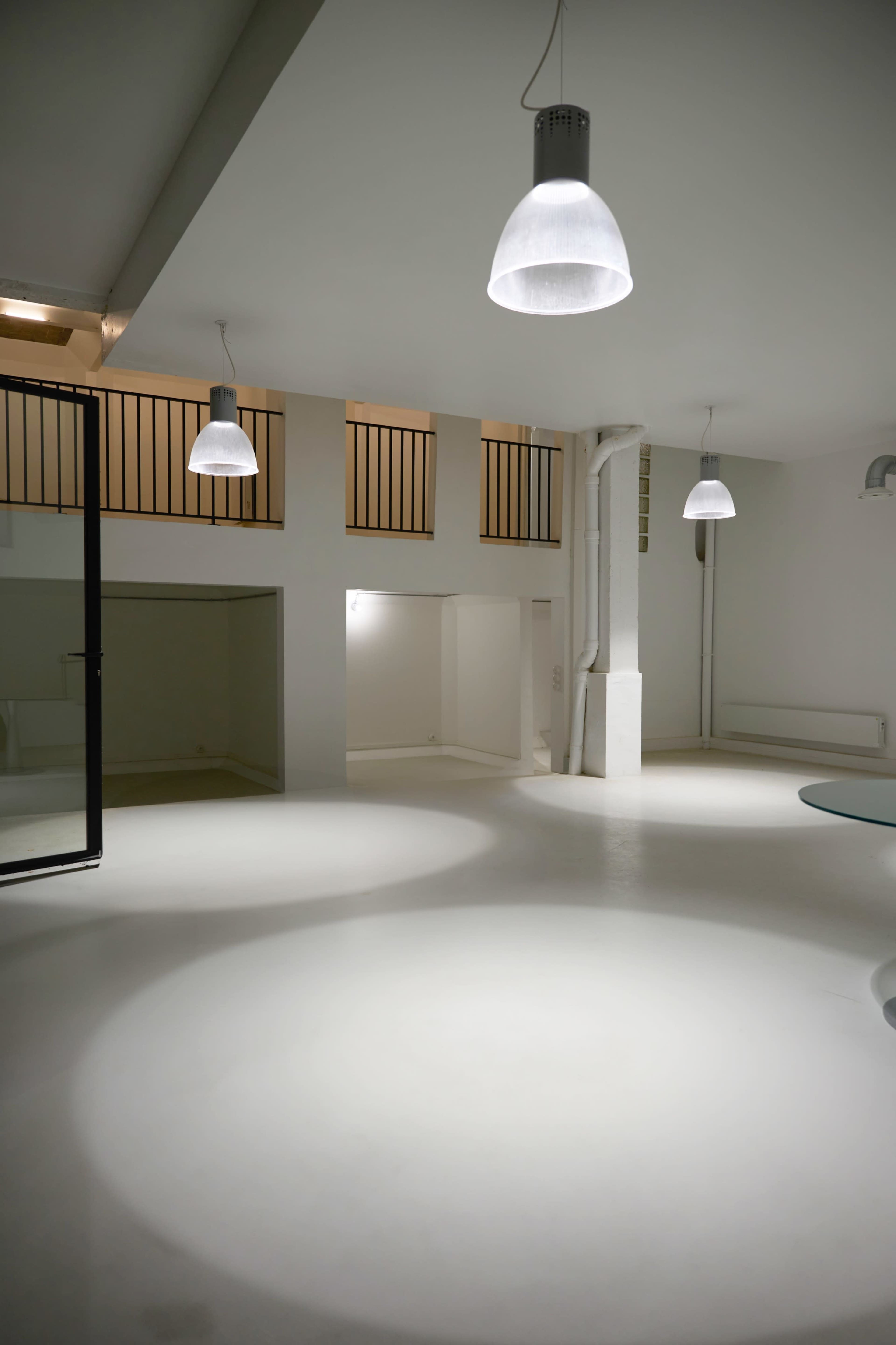 A minimalist, open interior space with white walls, a smooth floor, and several pendant lights hanging from the ceiling.