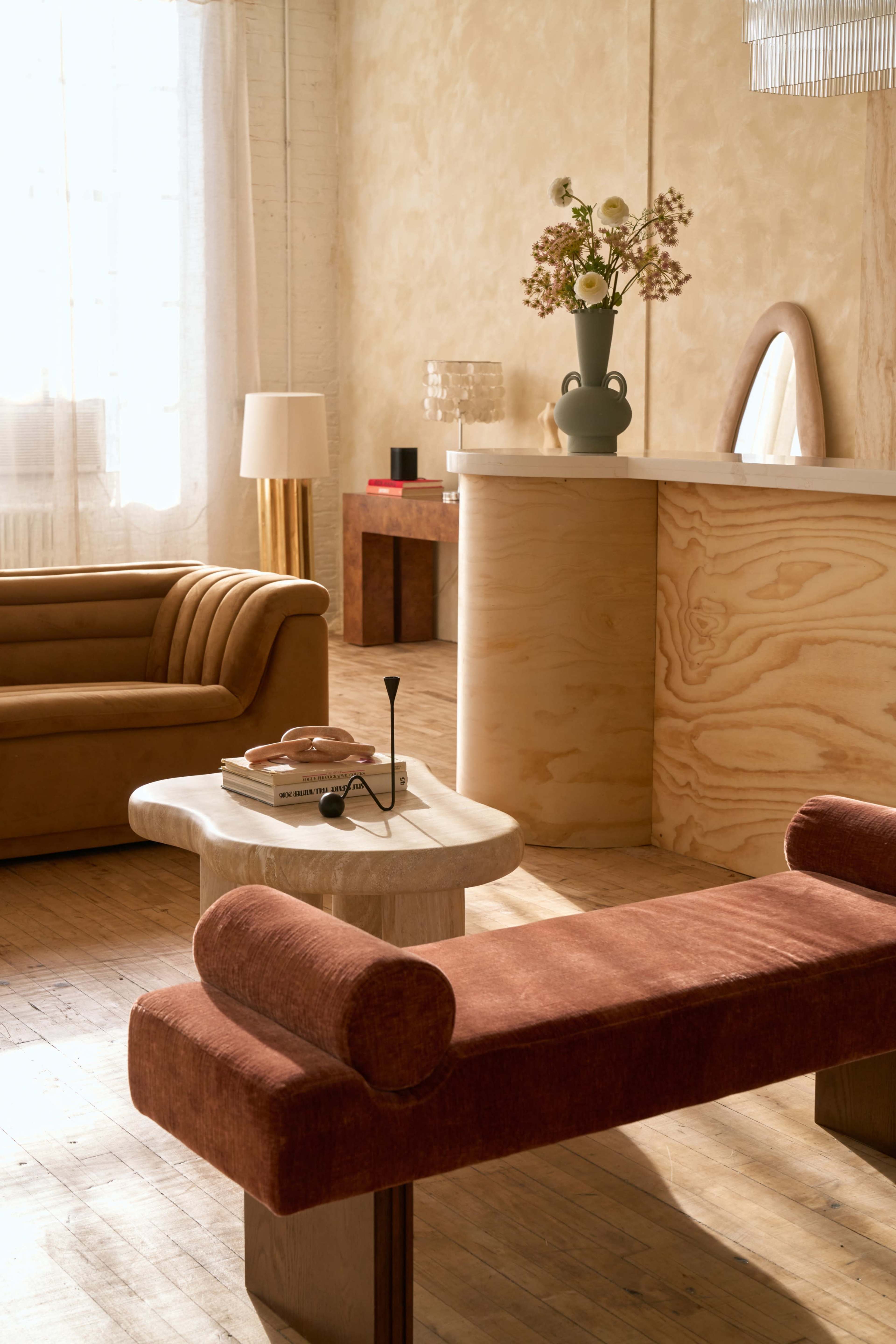 The image features a softly lit living room with a brown sofa, a rectangular table, and minimalist decor, including a vase of flowers and a lamp.