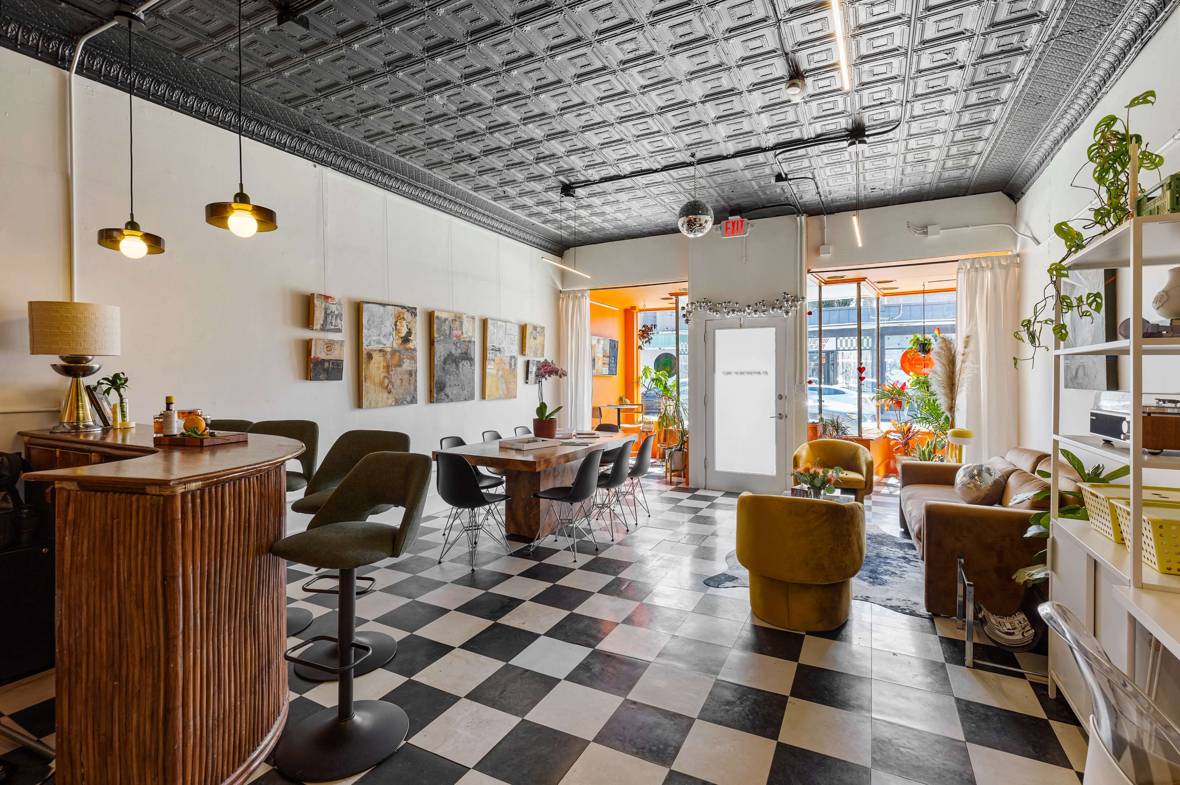 The image shows a stylish café interior with a bar area, dining tables, and large windows that open to the outside, featuring black and white checkered flooring and a decorative ceiling.