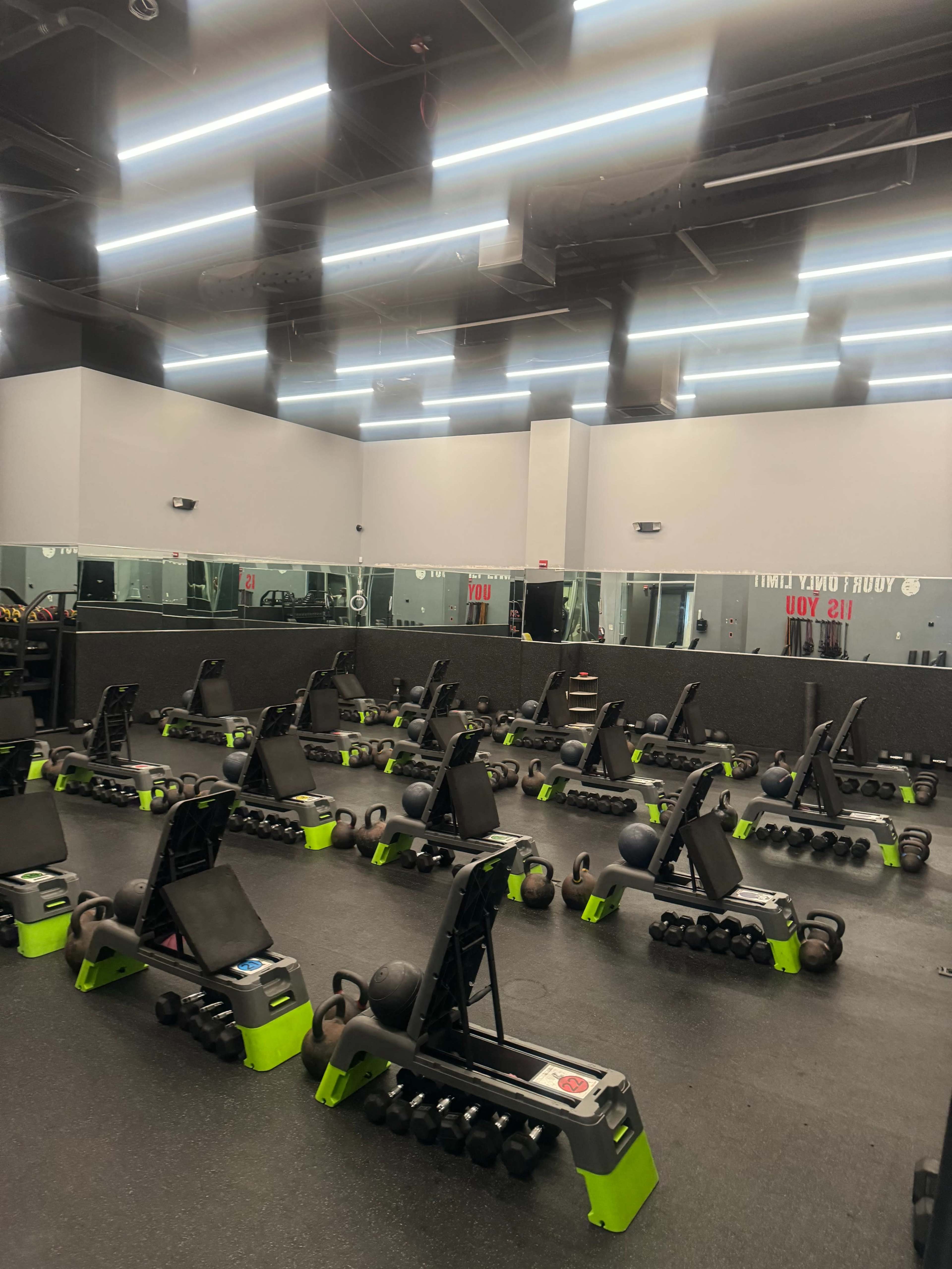 The image shows a fitness studio equipped with various weights, benches, and exercise mats organized neatly across the floor.