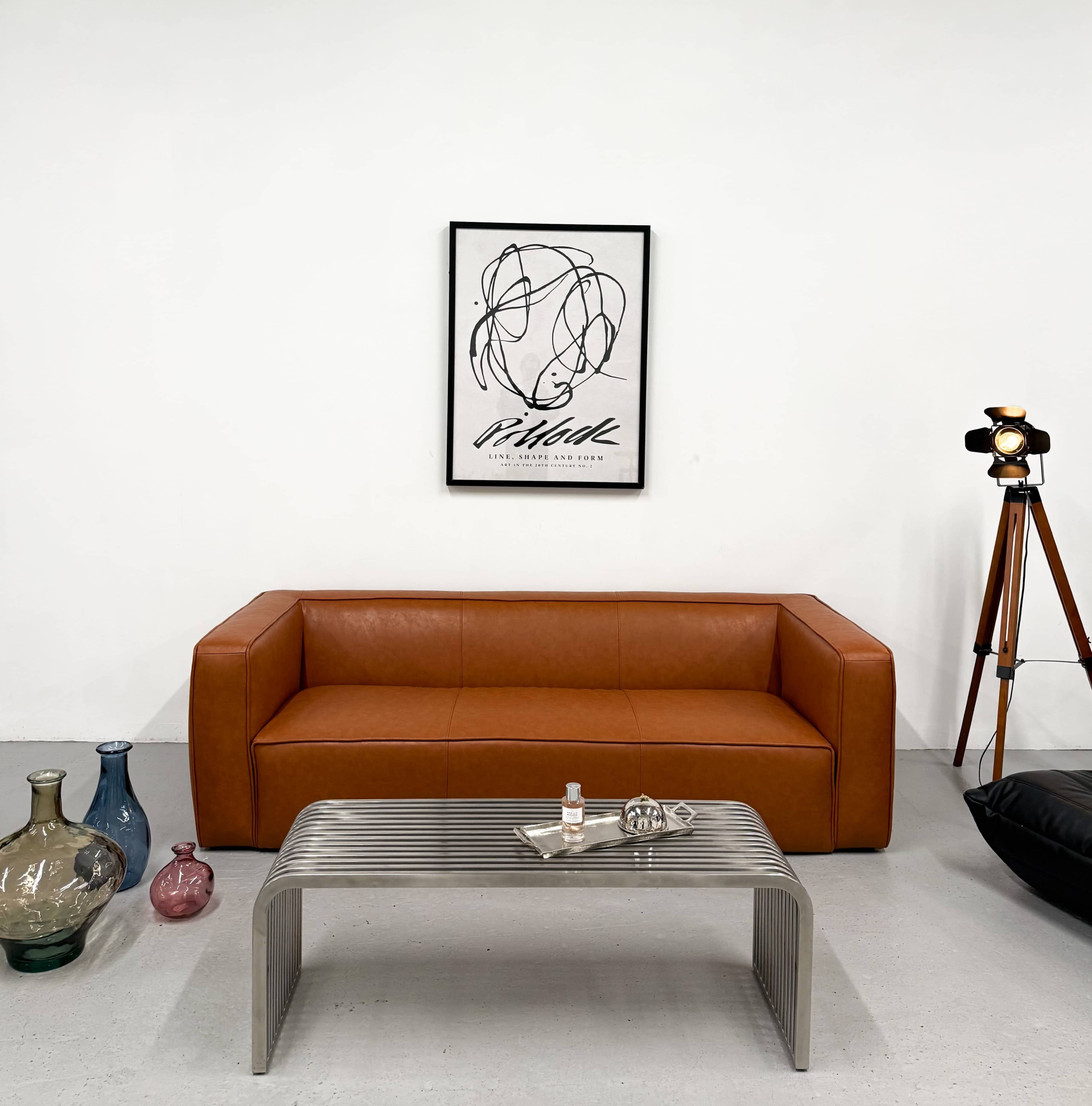 A modern living room features a brown leather sofa, a striped metal coffee table, and various decorative glass vases.