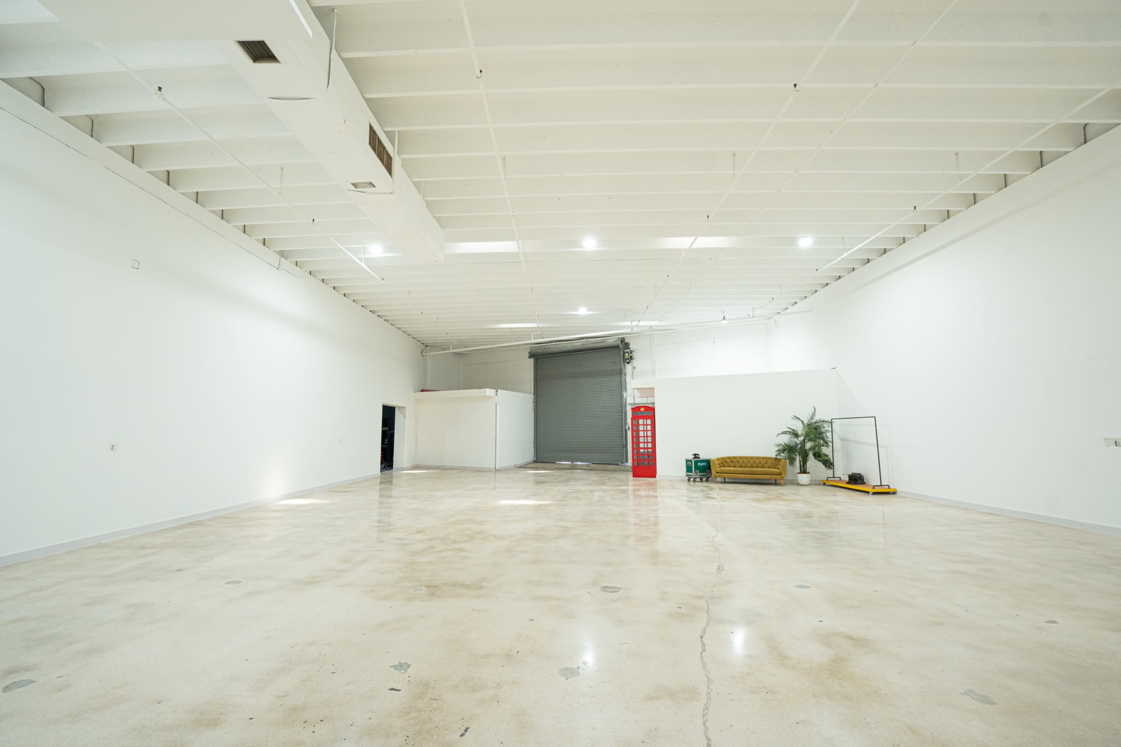 The image shows a large, empty industrial space with a polished concrete floor, white walls, and a gray roll-up door in the background.