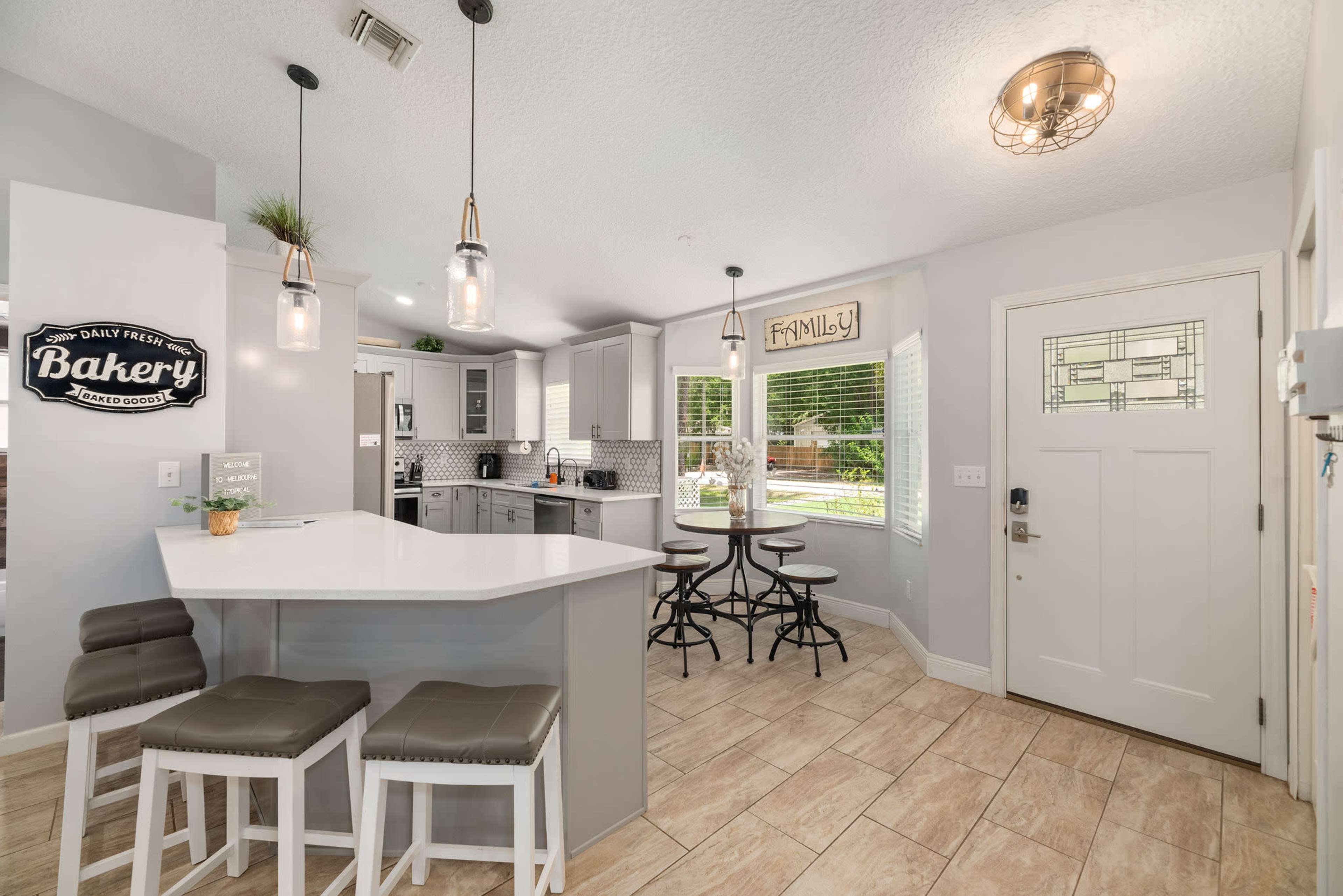A modern kitchen features a white island with bar seating, gray cabinets, and a dining area, with a door leading to the outside.