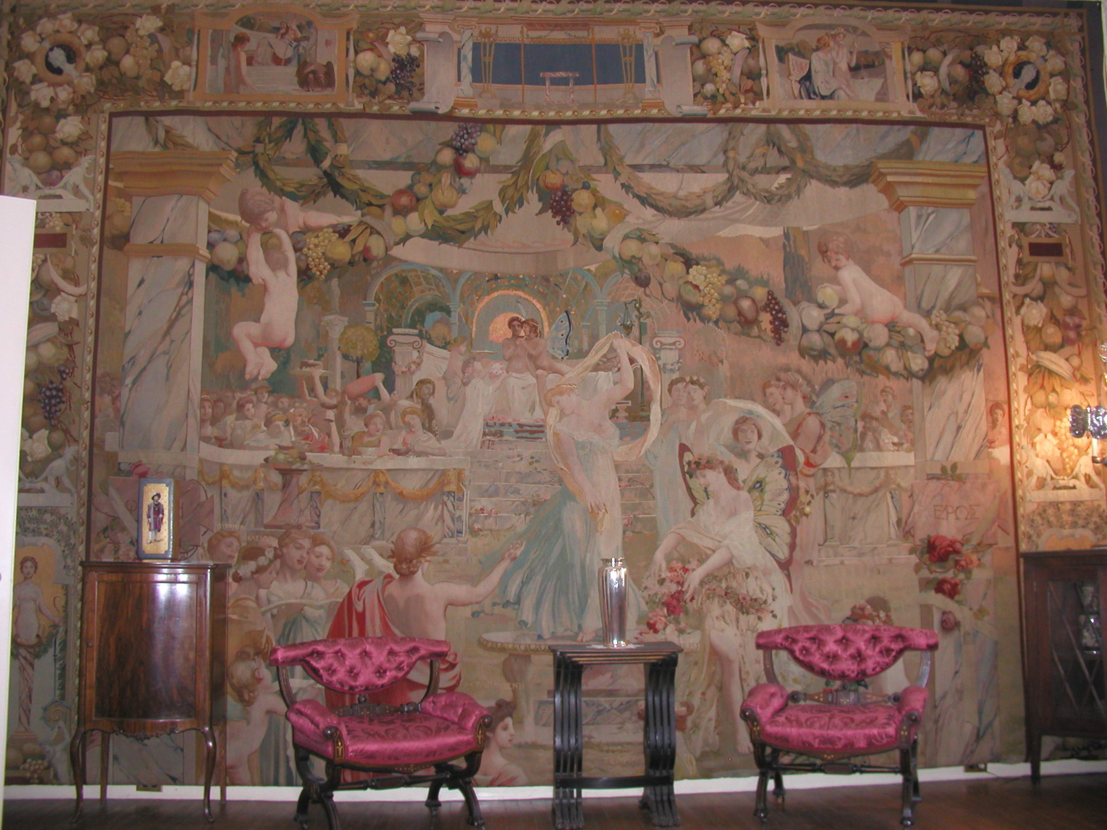 An ornate mural depicting a festive scene with figures celebrating around a central altar, flanked by two Victorian-style chairs.