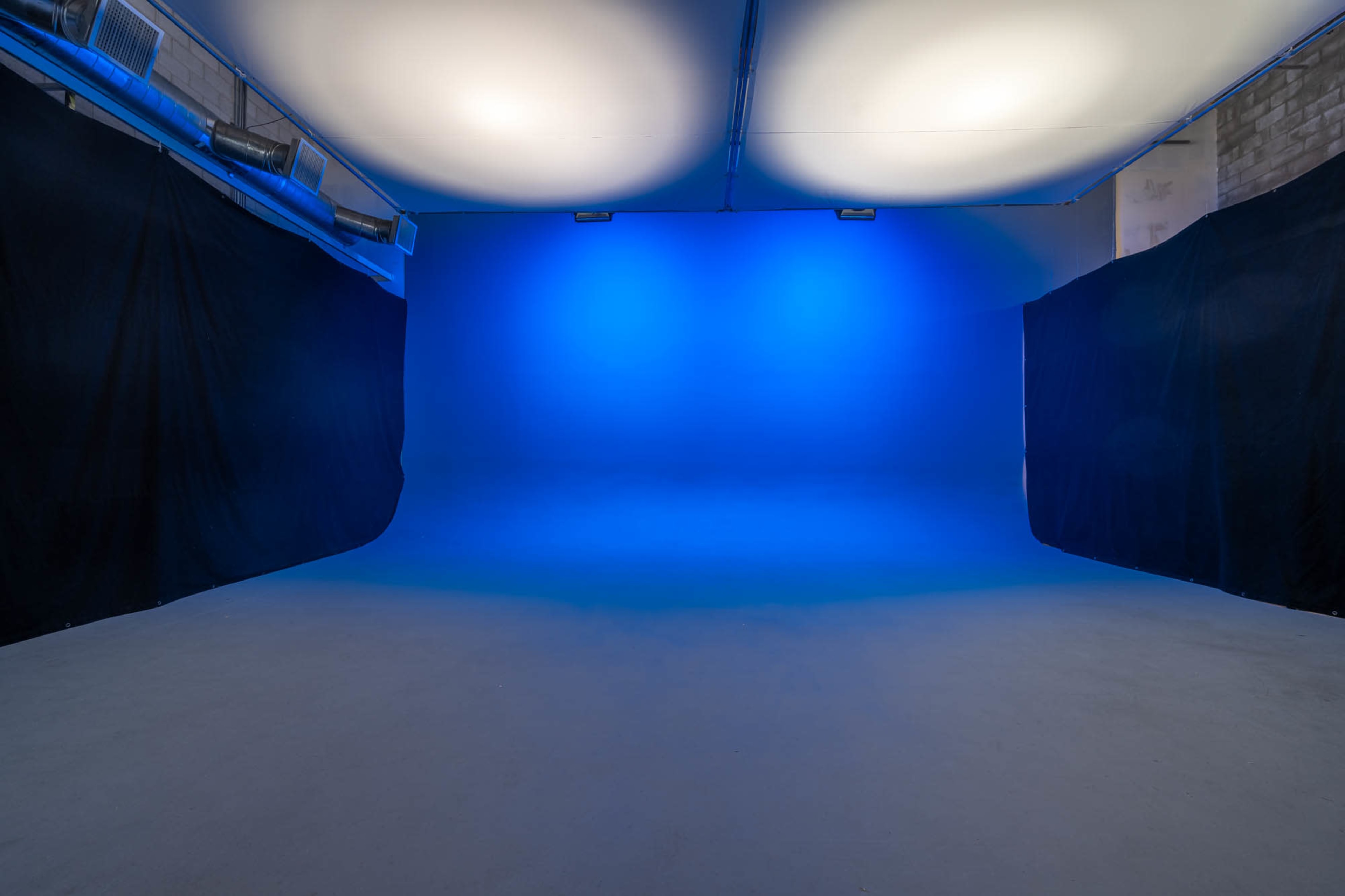 A blank photo studio with a blue backdrop and dark fabric draping on both sides.