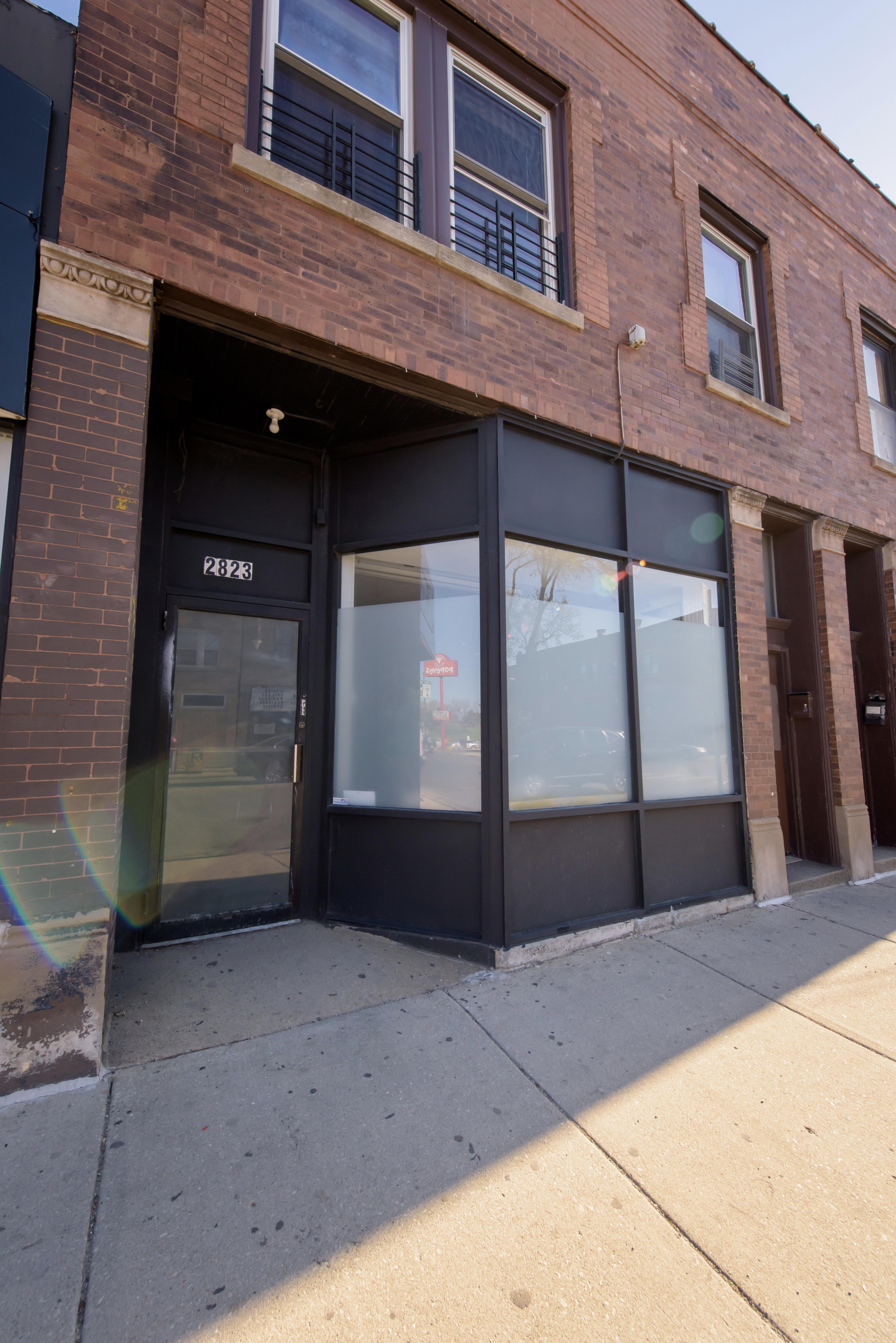 The image shows a brick building with a glass storefront located on a sidewalk.