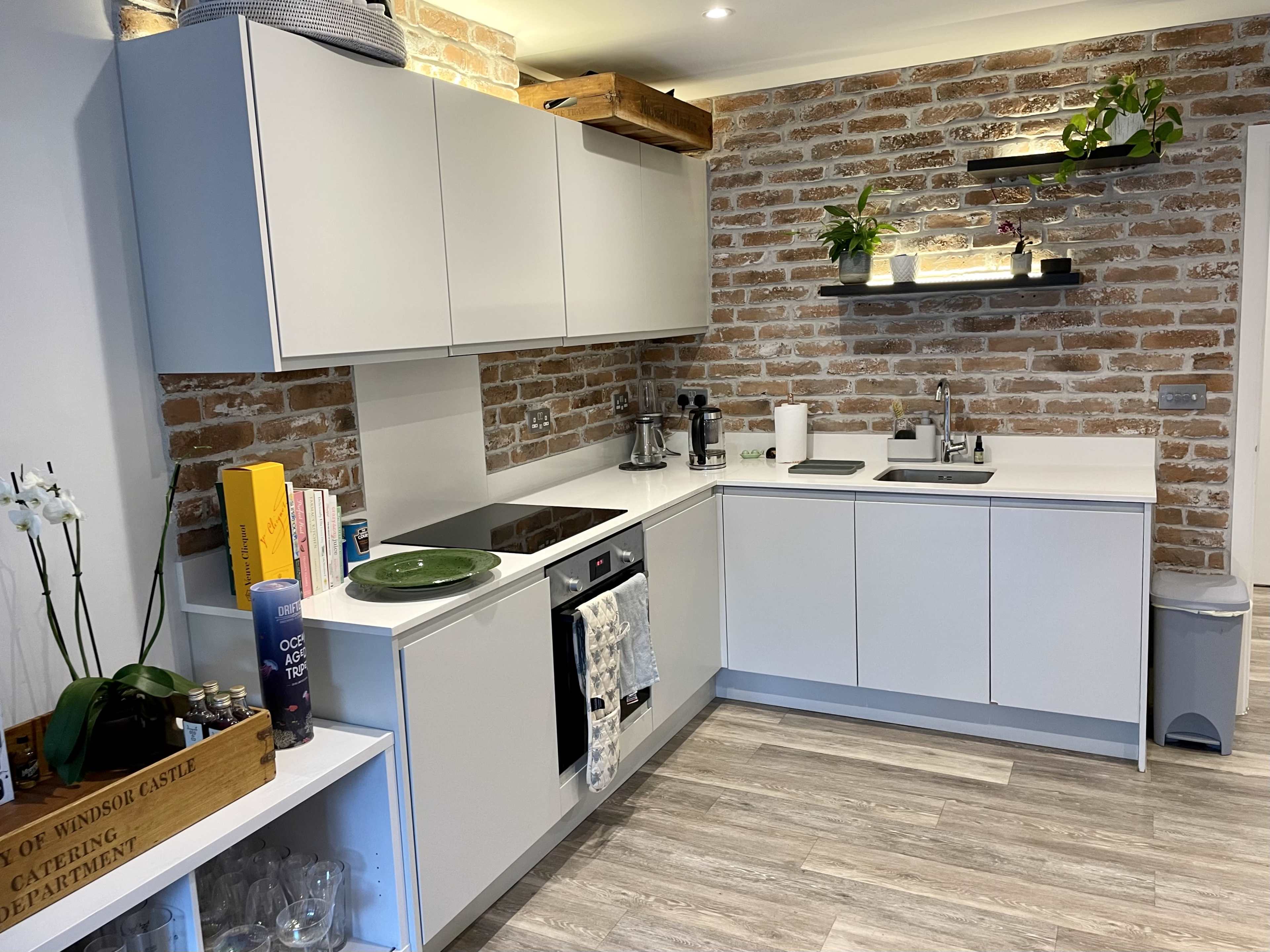 A modern kitchen with white cabinets, a brick wall, and a countertop featuring various appliances and plants.