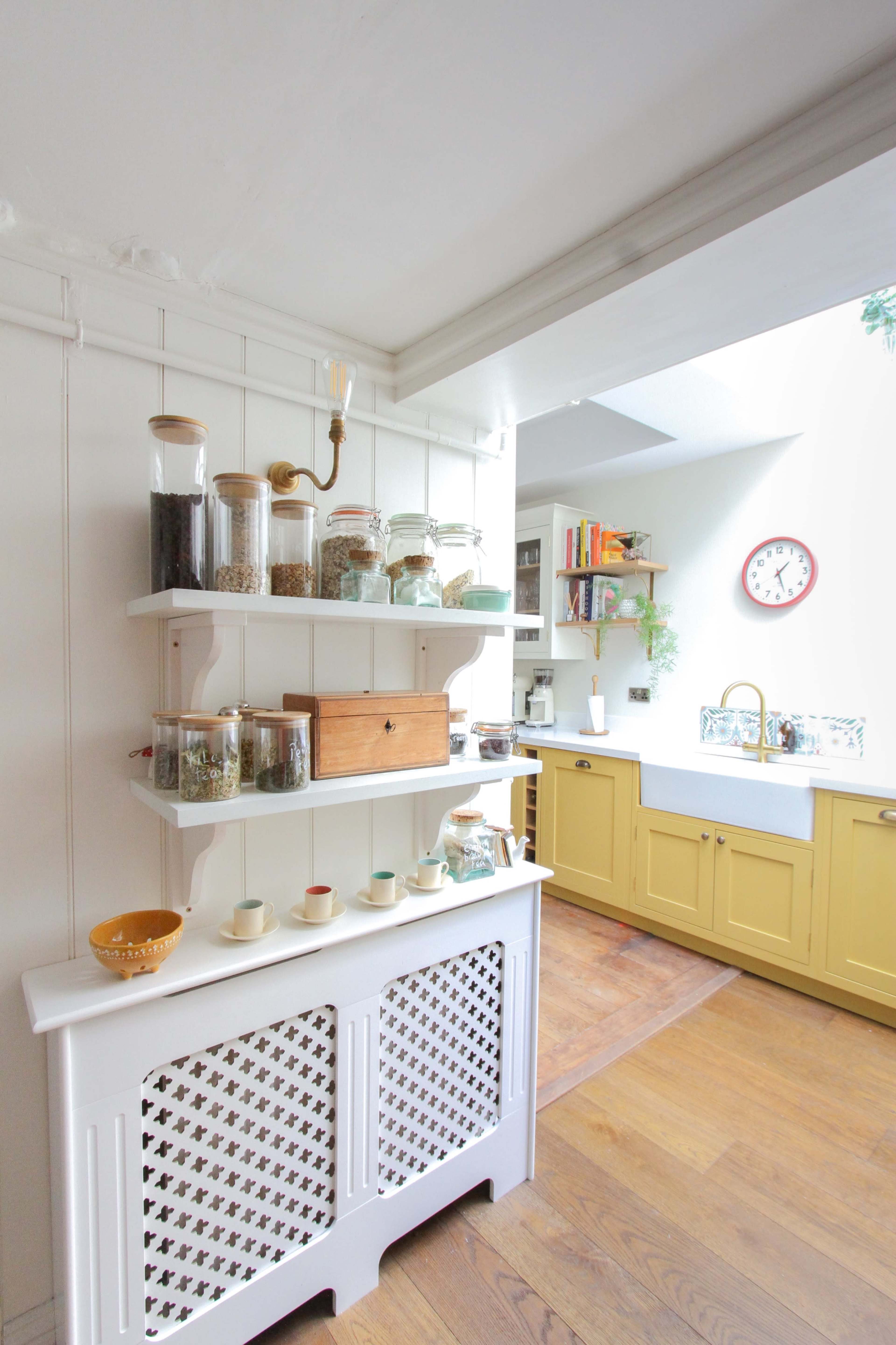 A kitchen area featuring a white storage unit with a patterned front, shelves filled with jars of spices and herbs, and yellow cabinetry in the background.