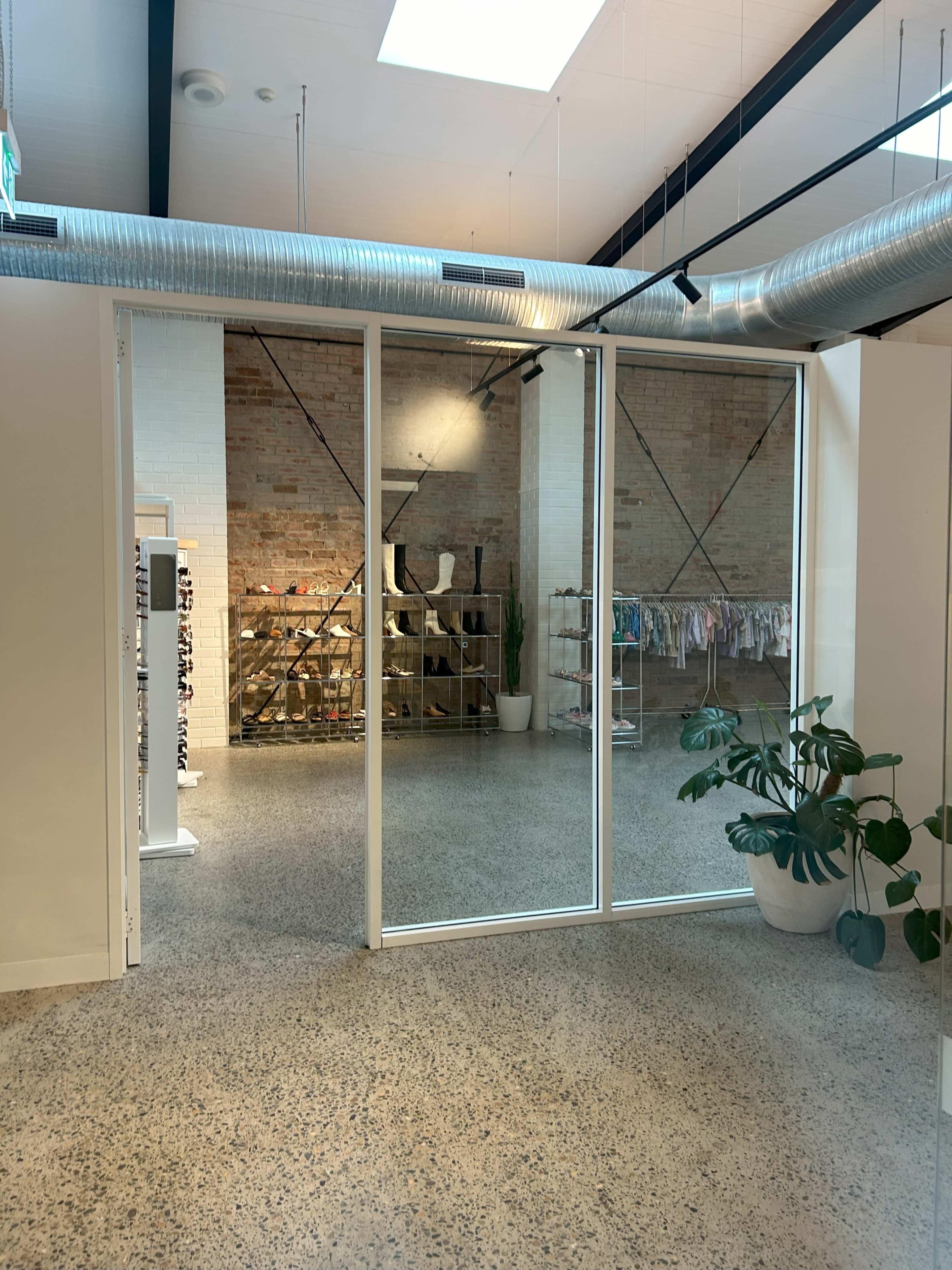 A spacious interior with glass sliding doors leading to a room featuring shelves of clothing and a large plant in the foreground.