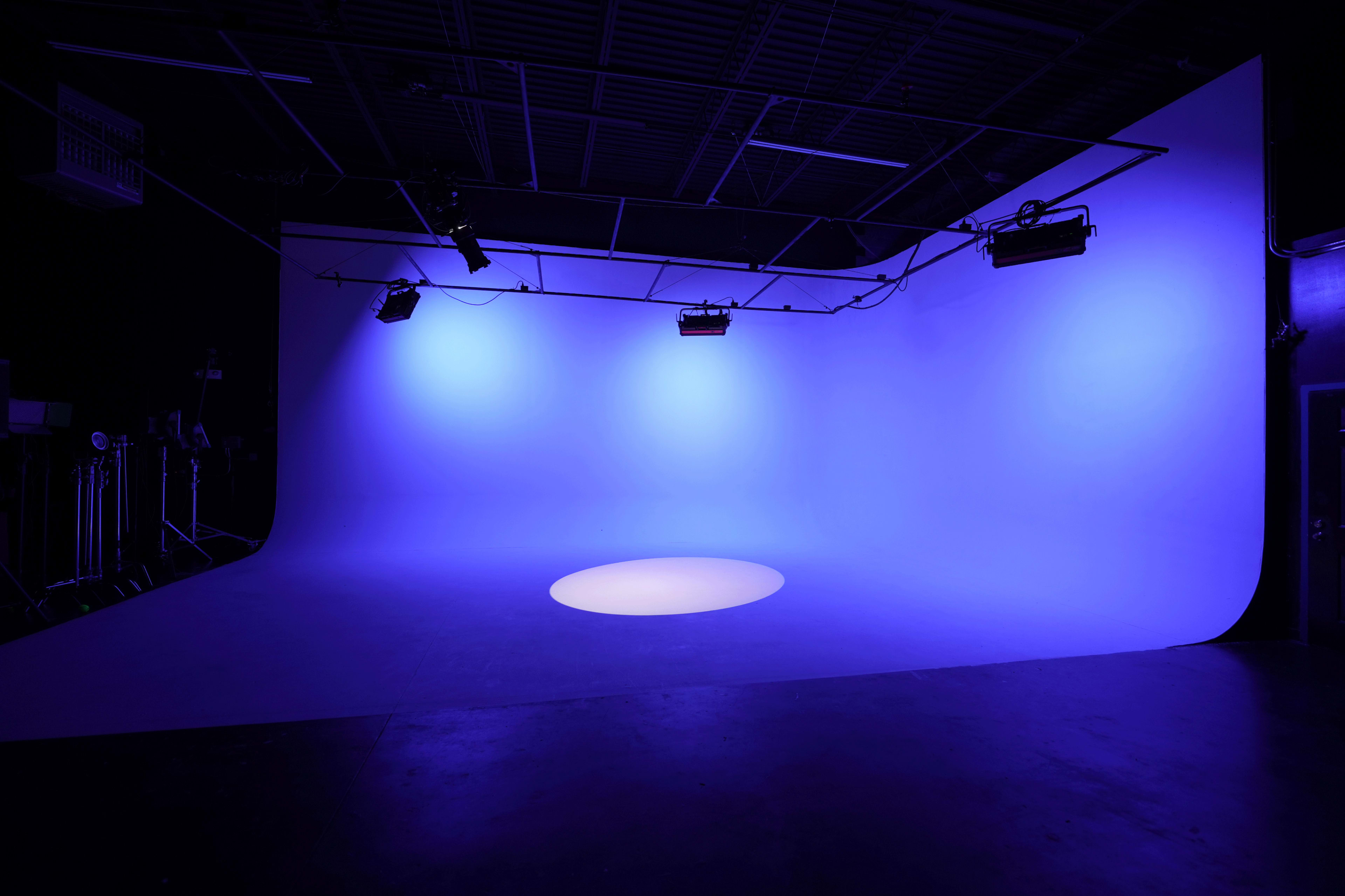 The image shows a photography studio with a seamless purple backdrop and a circular spotlight on the floor.