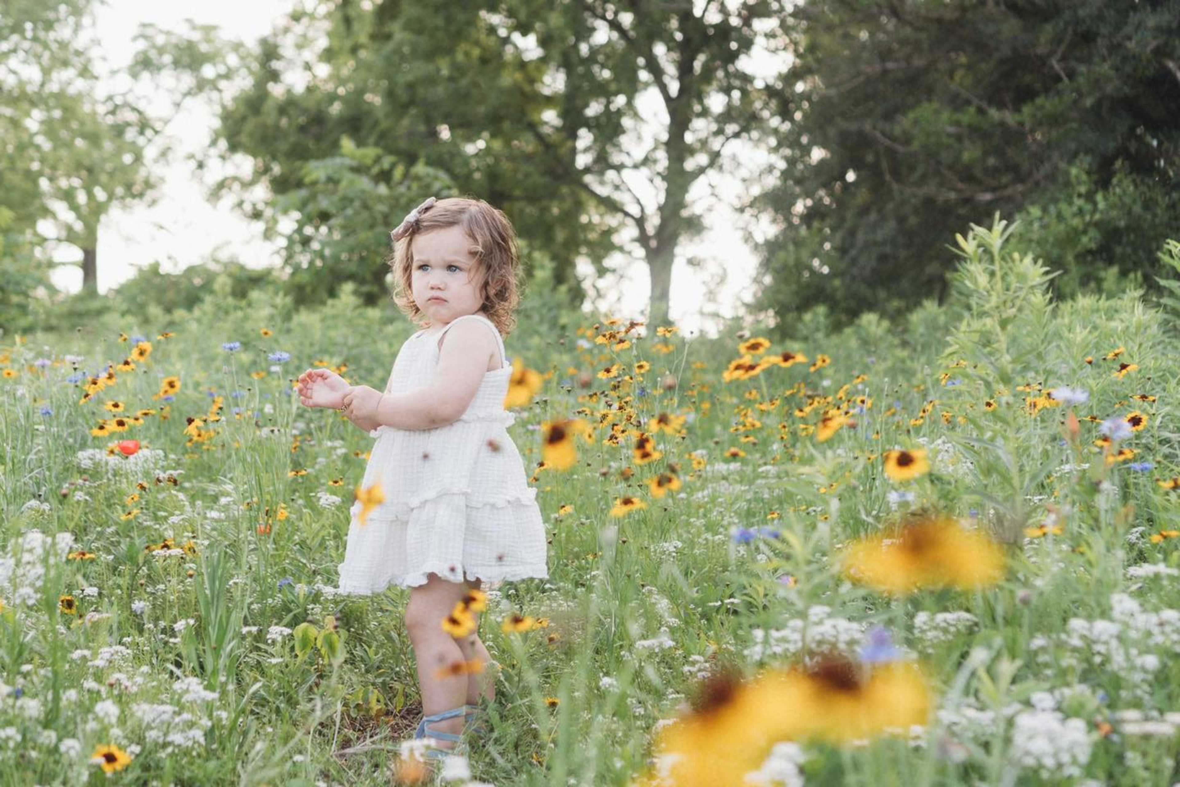 A young child in a white dress stands among a field of wildflowers.