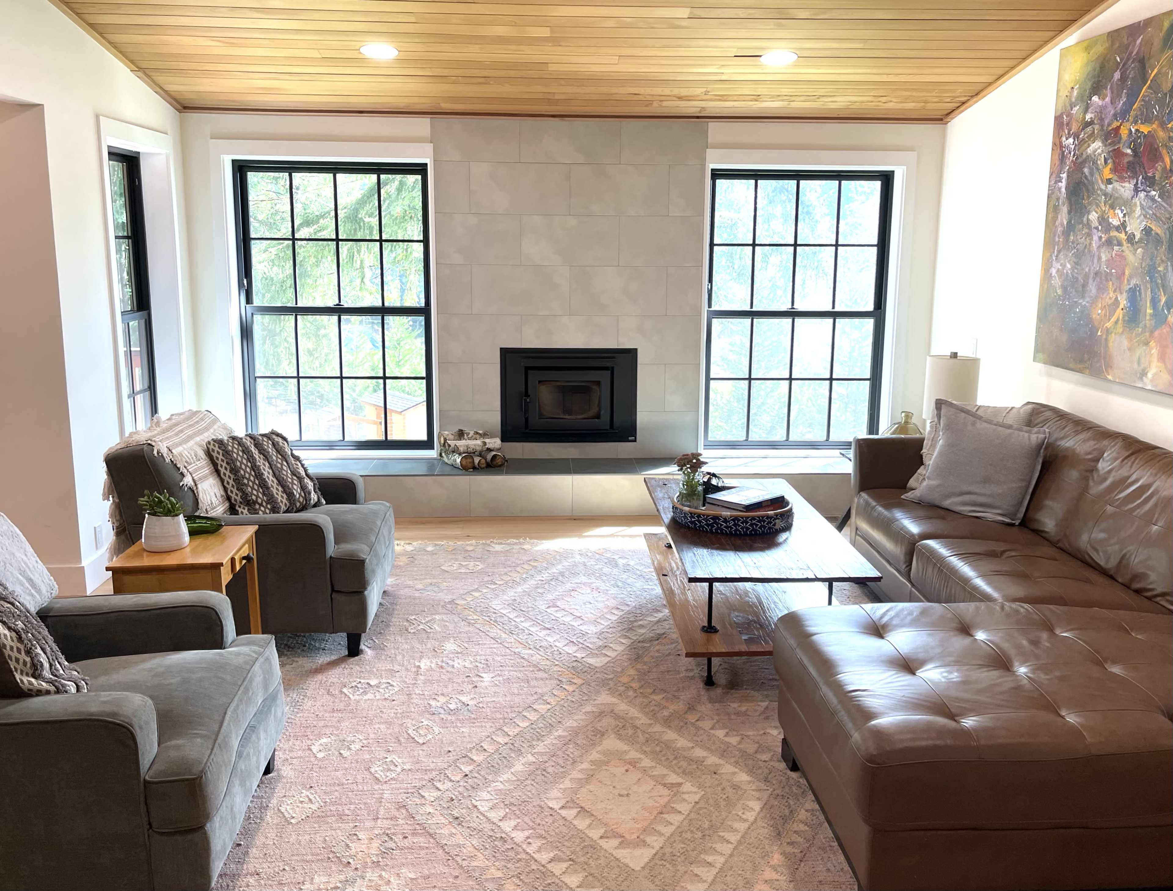 A modern living room featuring a fireplace centered between two windows, with a sofa, armchairs, and a coffee table on a patterned rug.