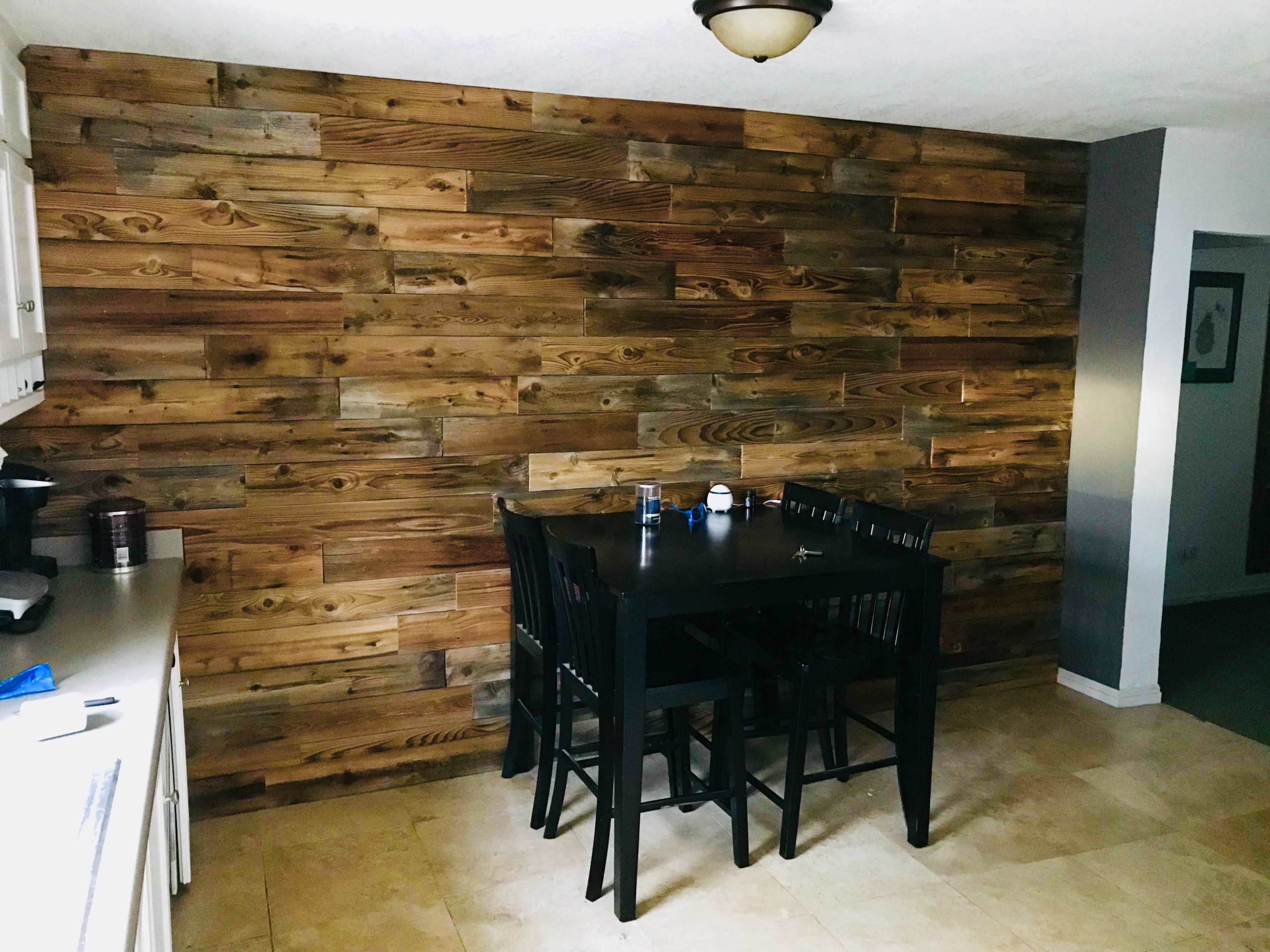 A dining area with a wooden wall feature and a black table set with four chairs.