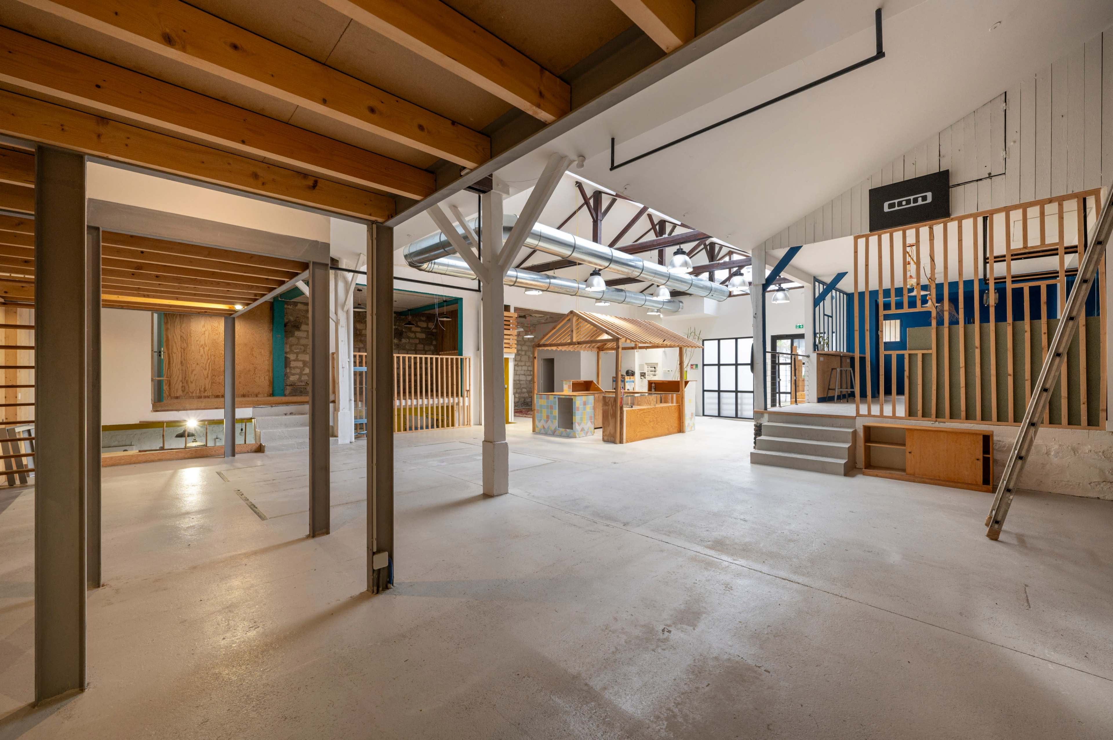 An open, spacious interior of a renovated building with wooden beams, various structures, and staircases.