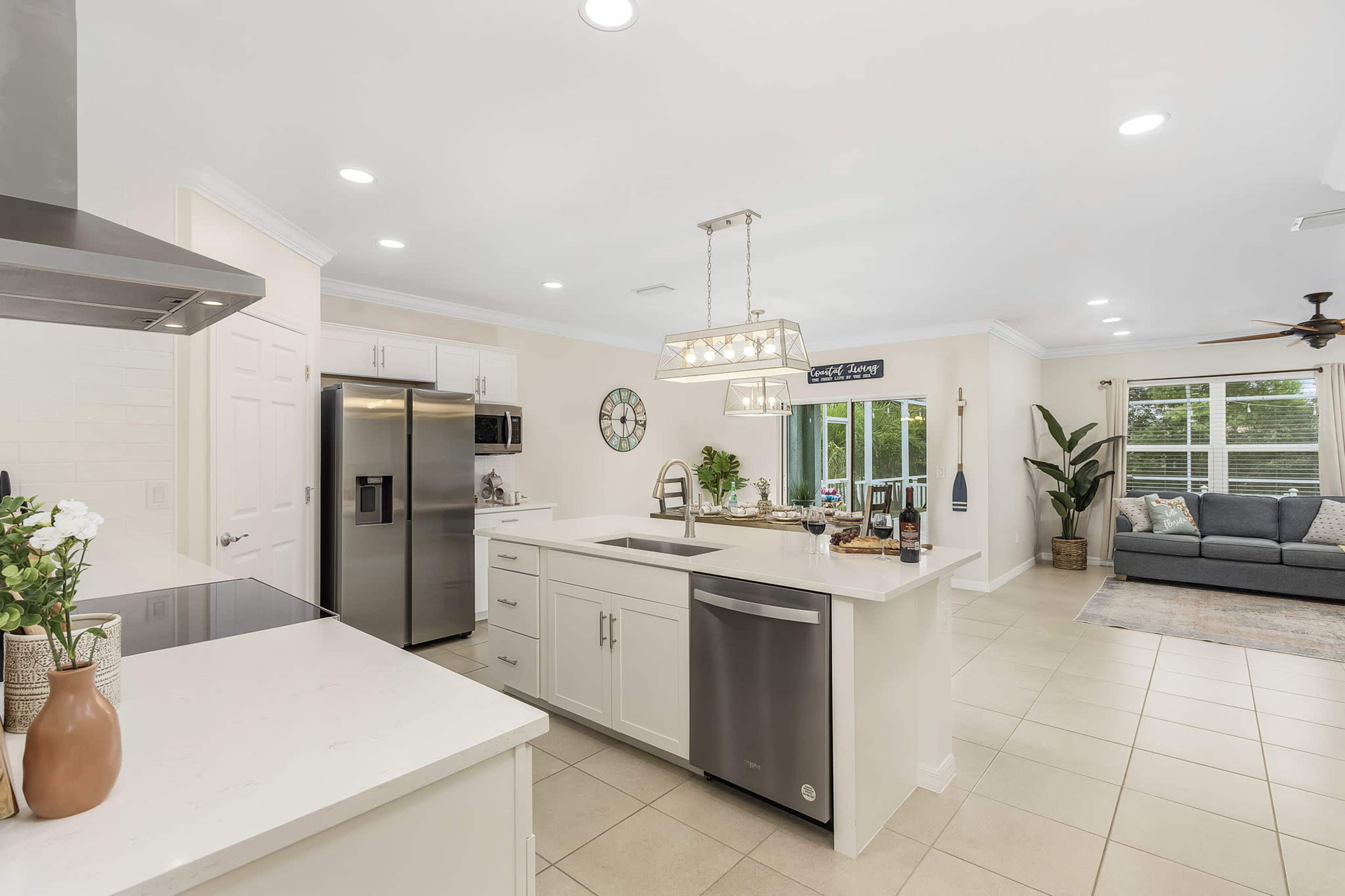 A modern kitchen features stainless steel appliances, a center island with a sink, and a dining area with a view of a living room.