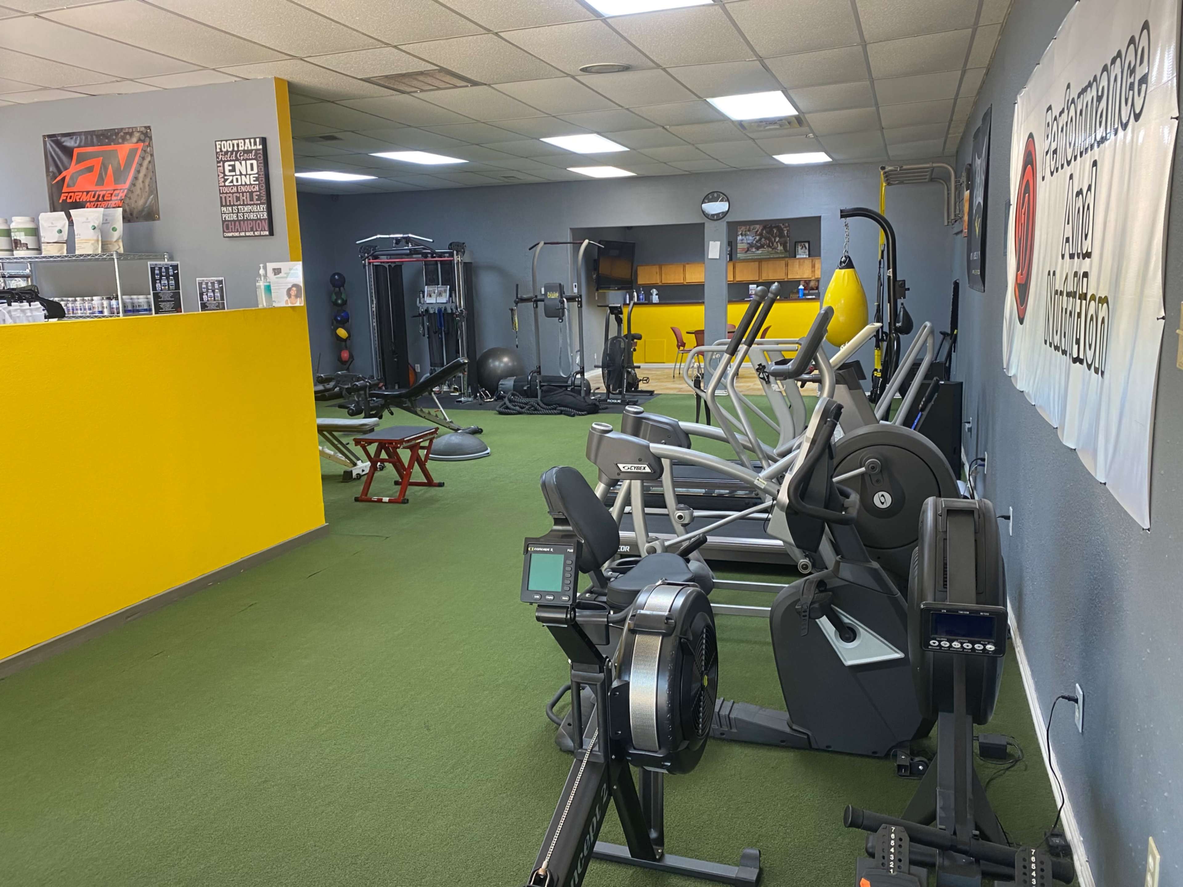 A fitness facility equipped with various exercise machines, weights, and gym accessories on a synthetic green turf floor.