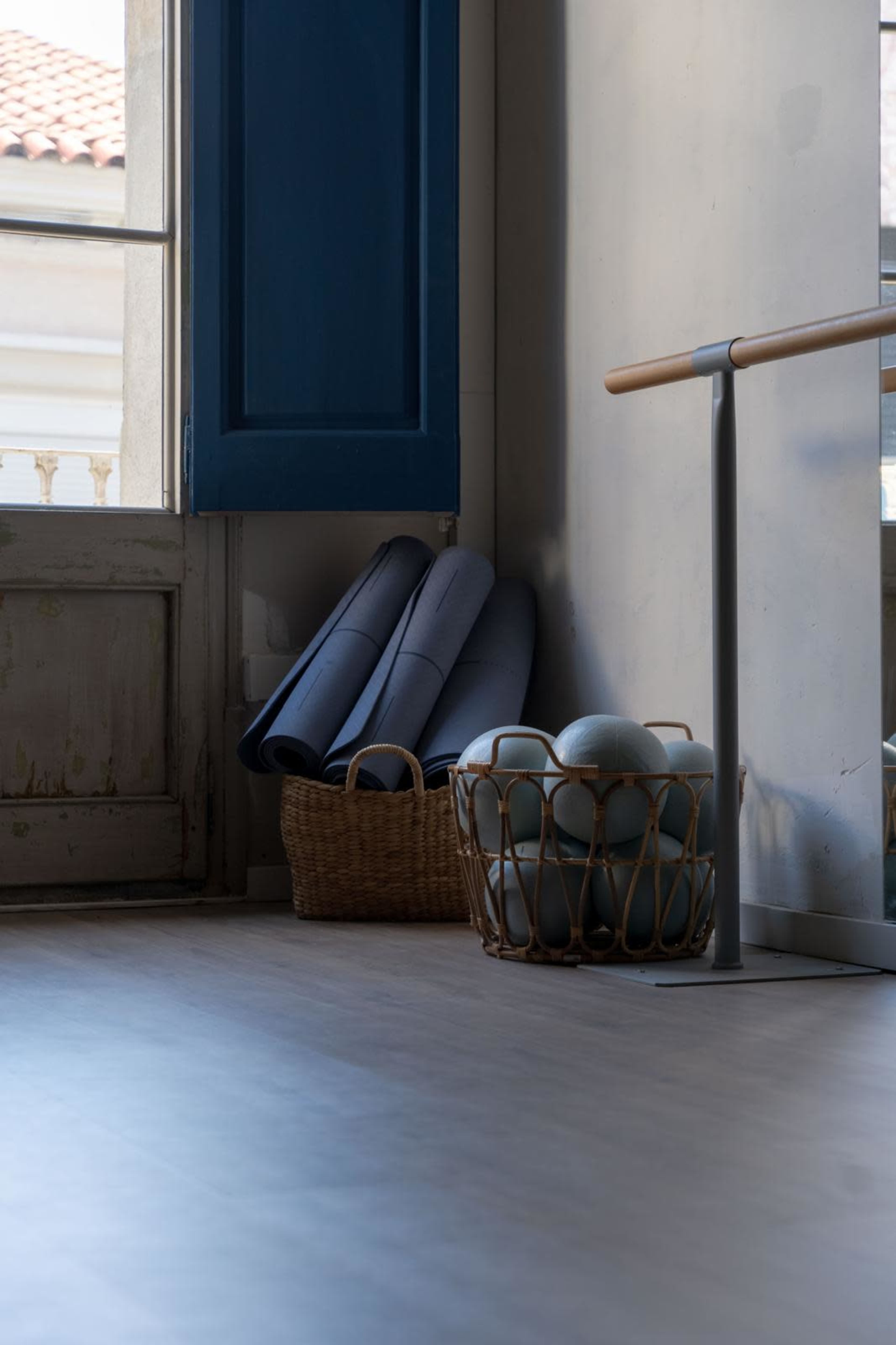The image shows a corner of a room with blue shutters, a basket containing exercise balls and rolled-up mats.