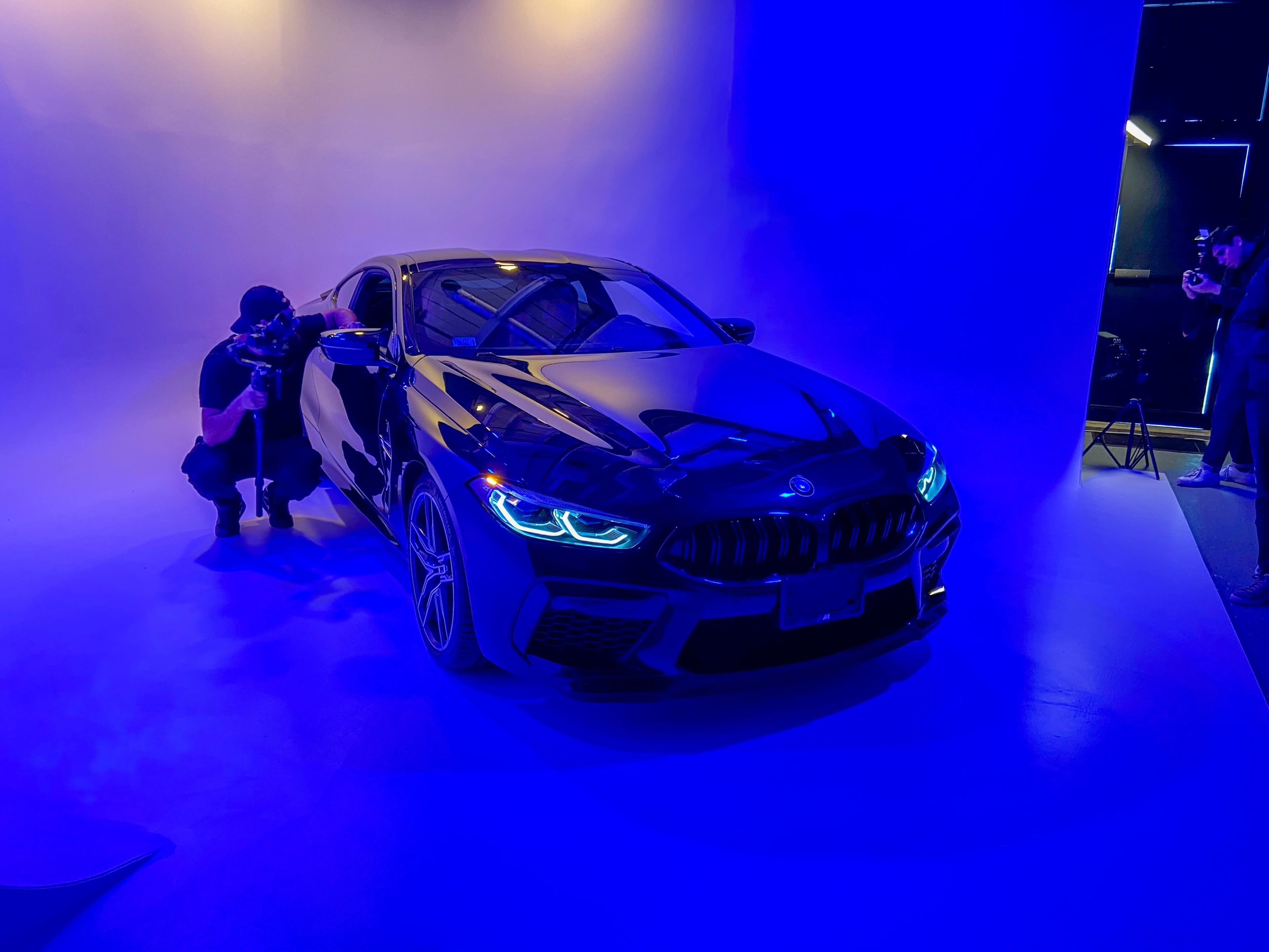 A photographer captures images of a black BMW car illuminated by blue lighting in a studio setting.