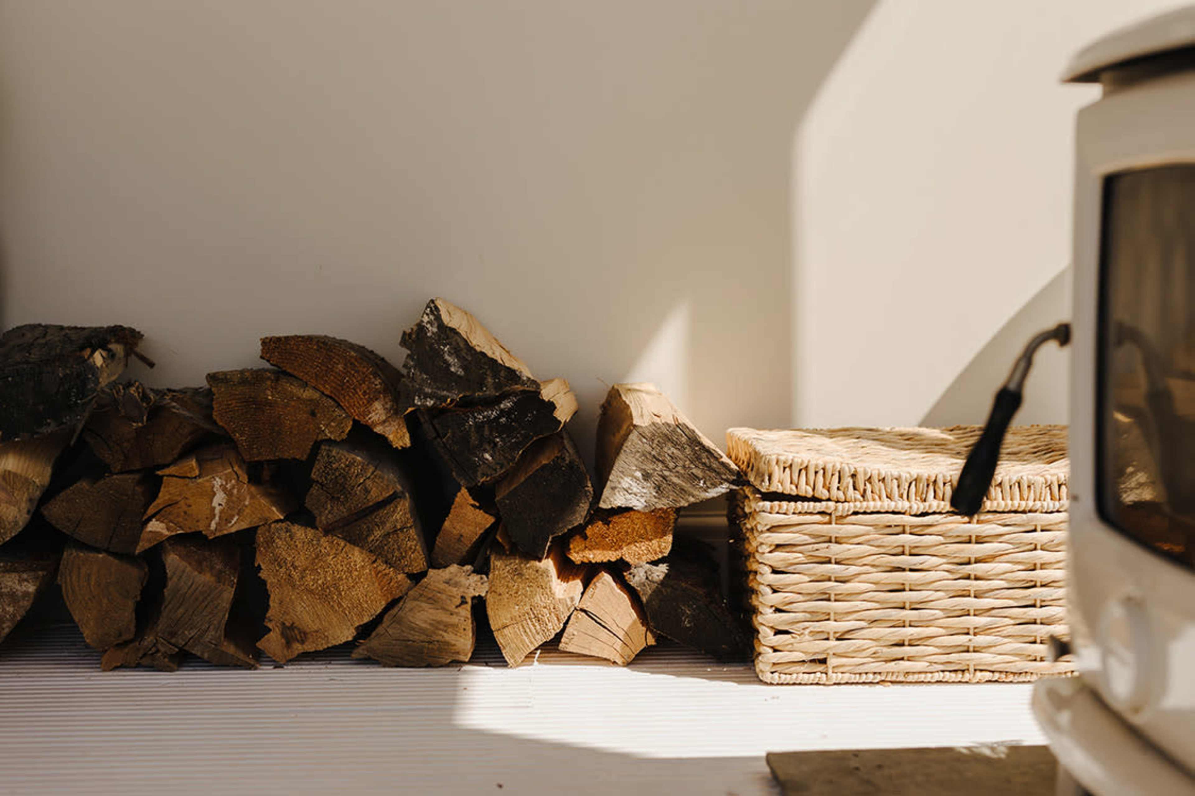 A stack of firewood next to a woven basket beside a white stove.