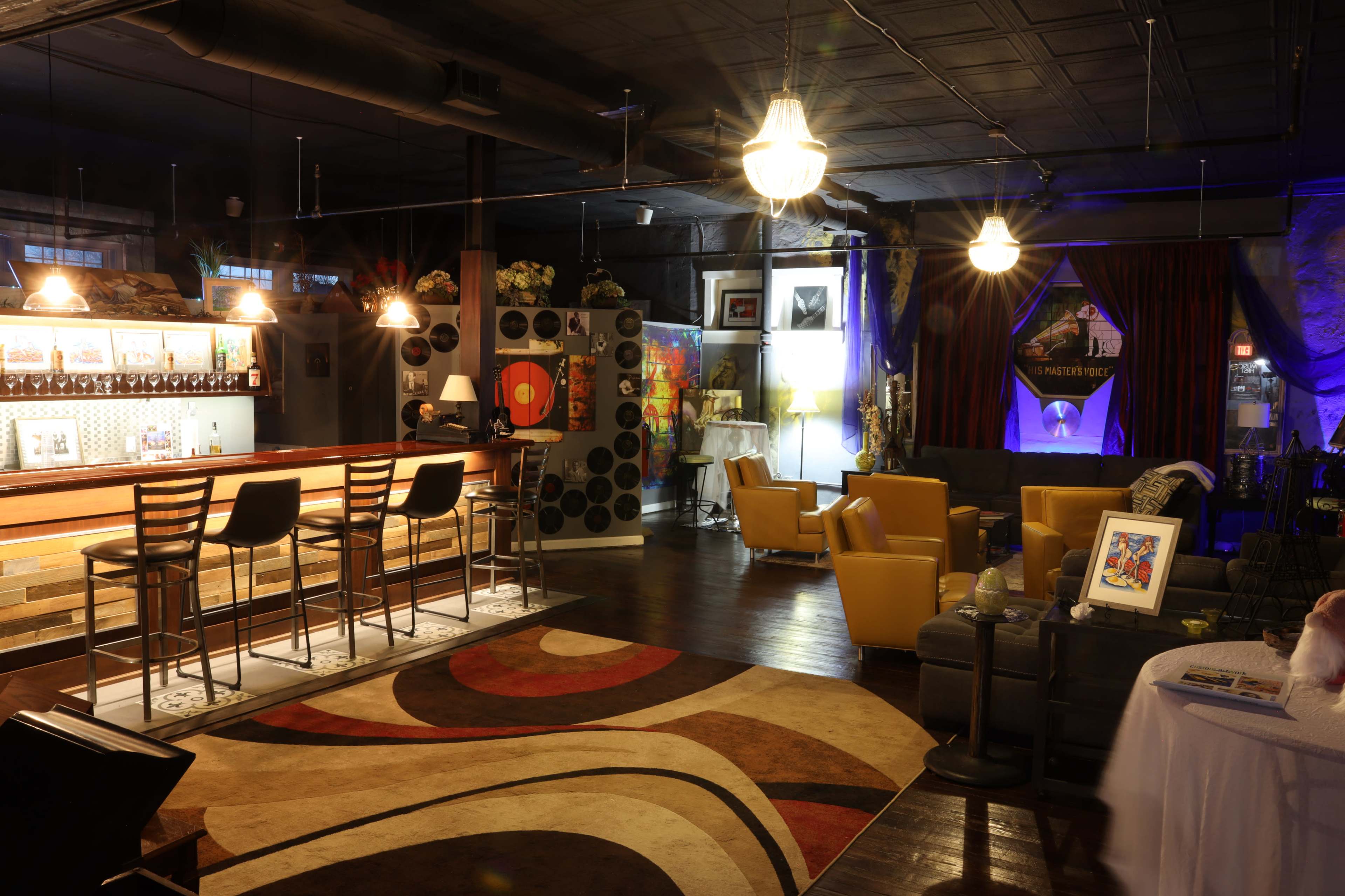 A stylish lounge area featuring a bar with high chairs, cozy seating arrangements, and decorative lighting.