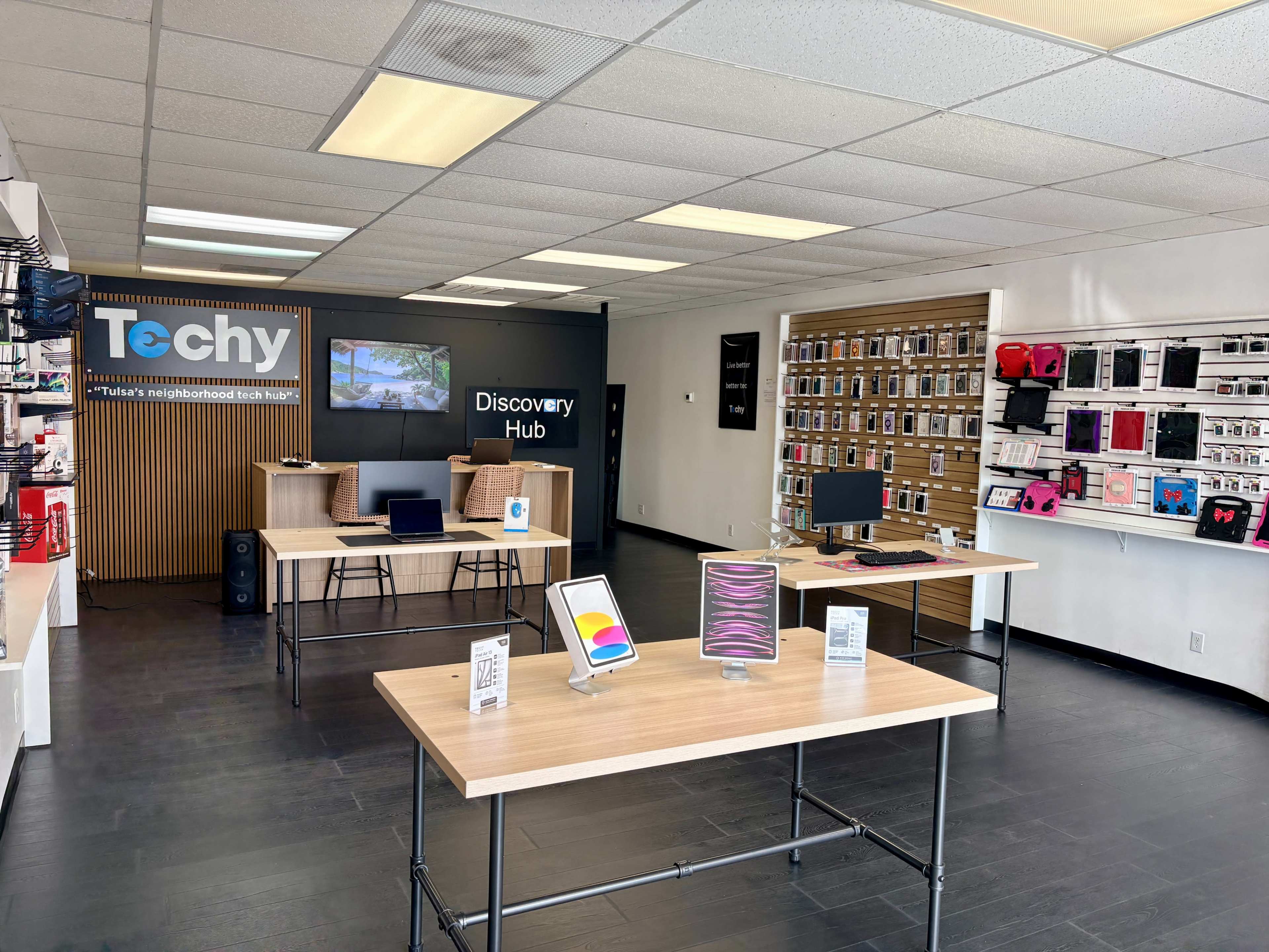 The image shows an interior of a tech retail store featuring displays with electronic devices, a large wall-mounted screen, and various tech accessories arranged on shelves.