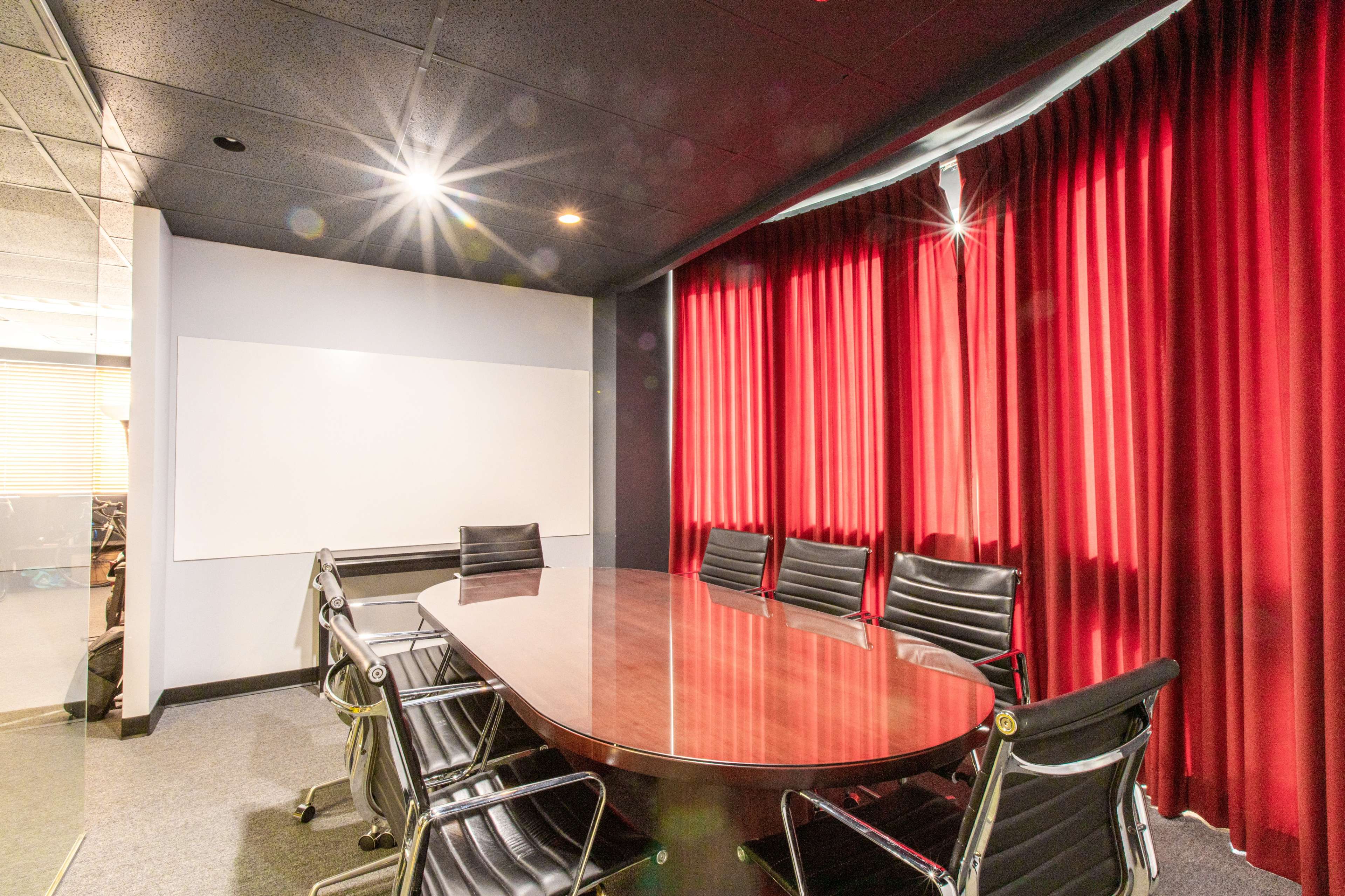 A conference room features a round wooden table surrounded by black leather chairs and red curtains.