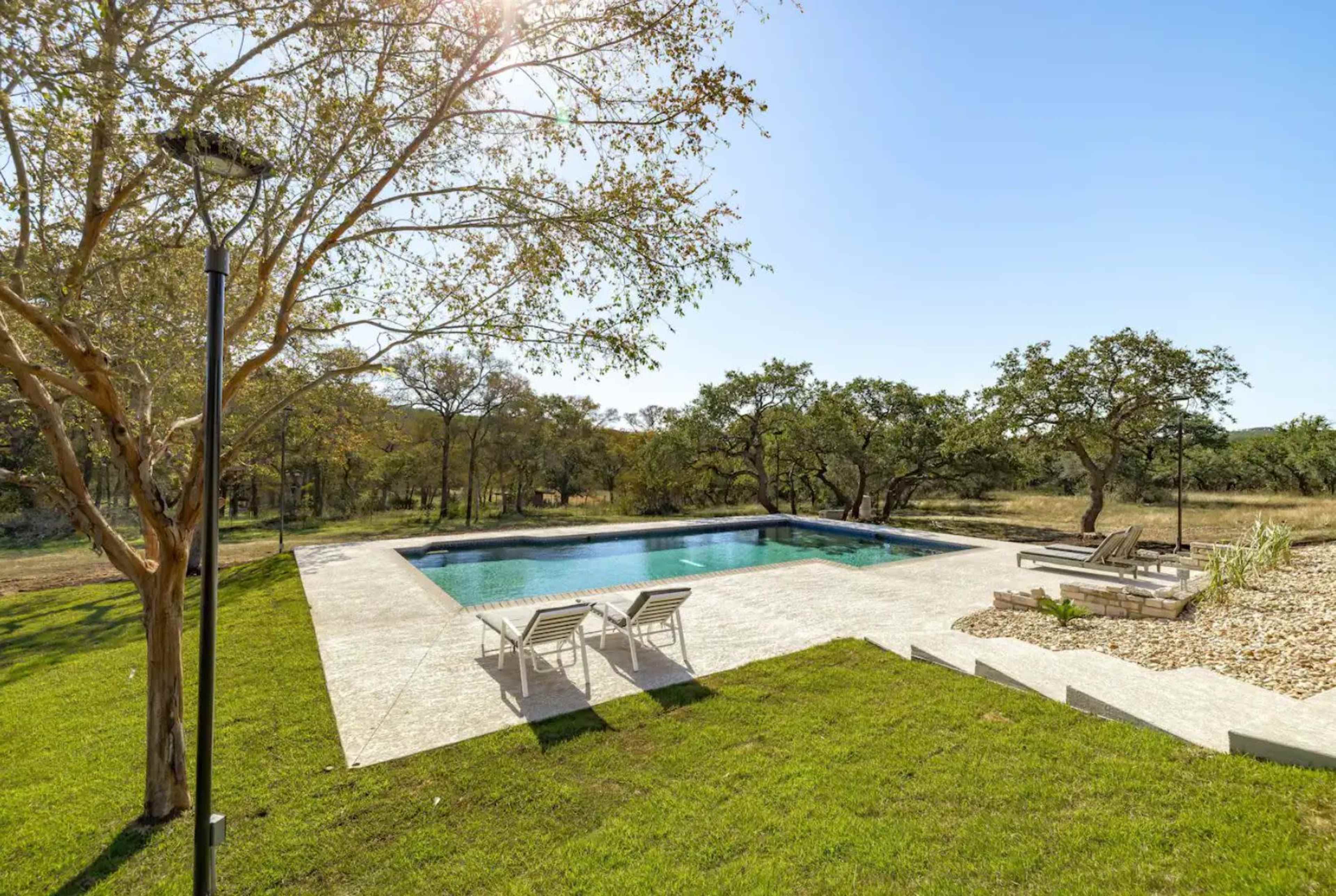 The image shows a spacious outdoor area featuring a swimming pool surrounded by a lawn and trees.