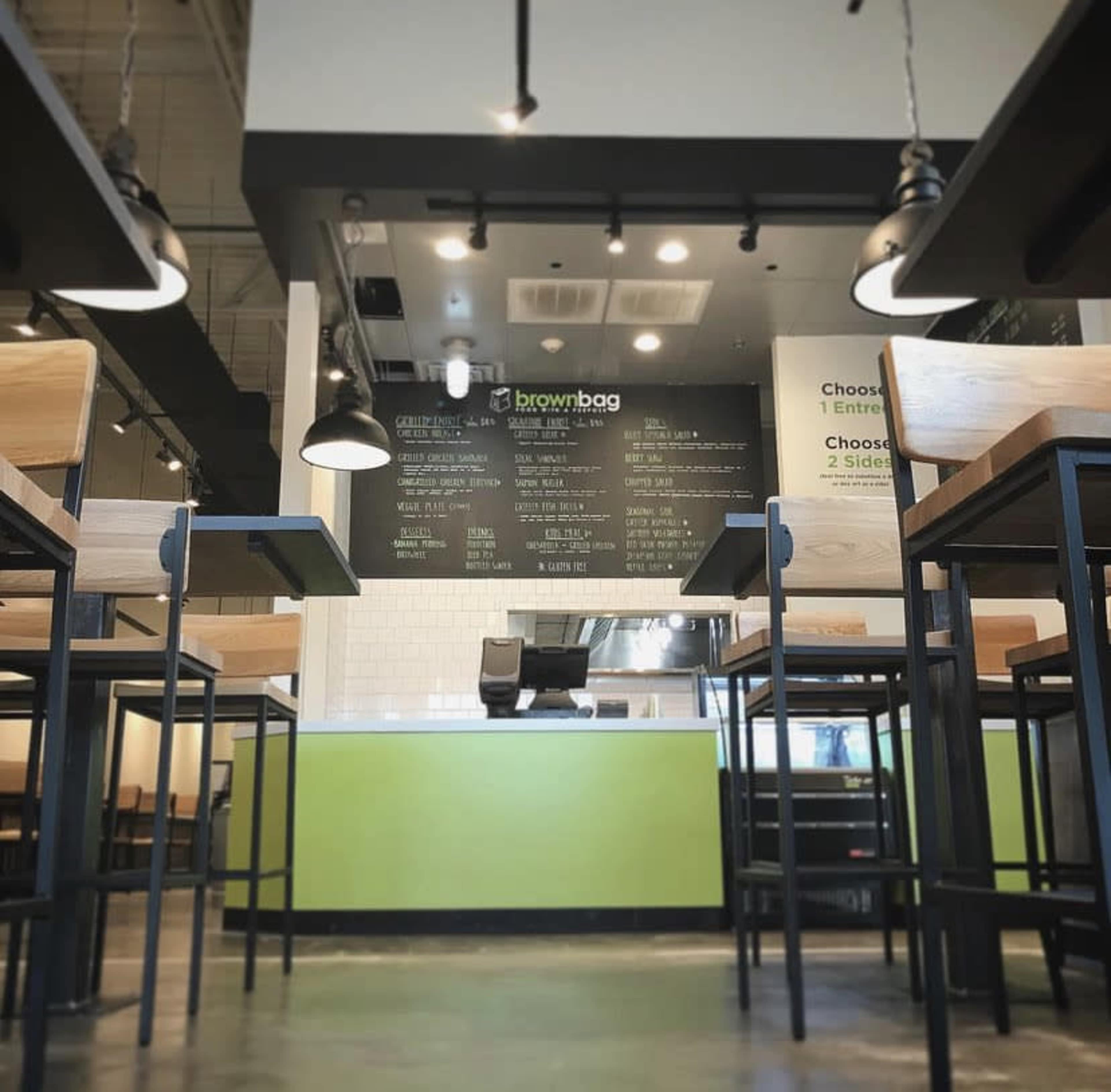 The interior of a café featuring metal-framed tables and a menu displayed on the wall above the service counter.