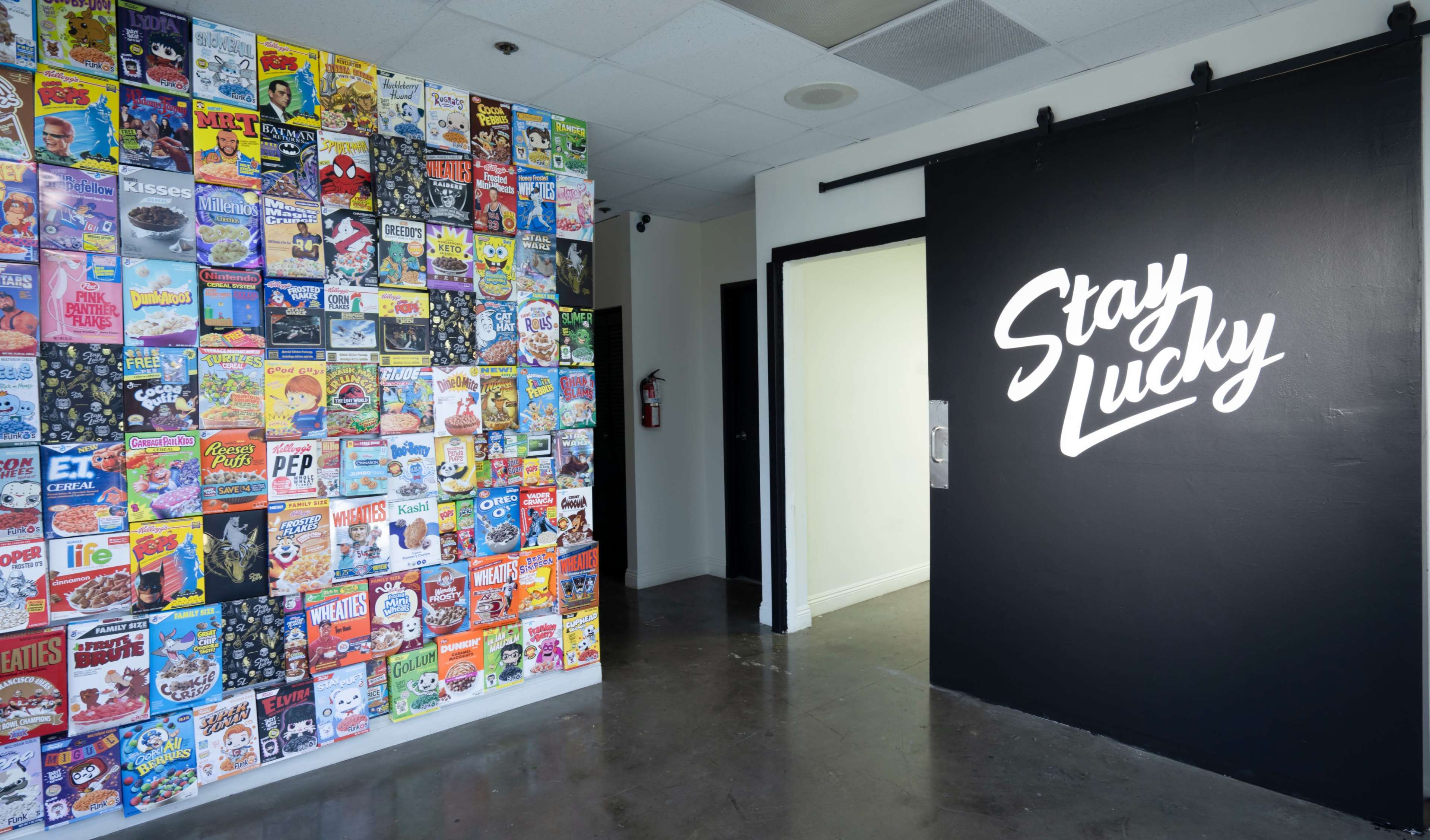 A wall covered with various cereal box designs next to a black wall with the words "Stay Lucky" written in white.