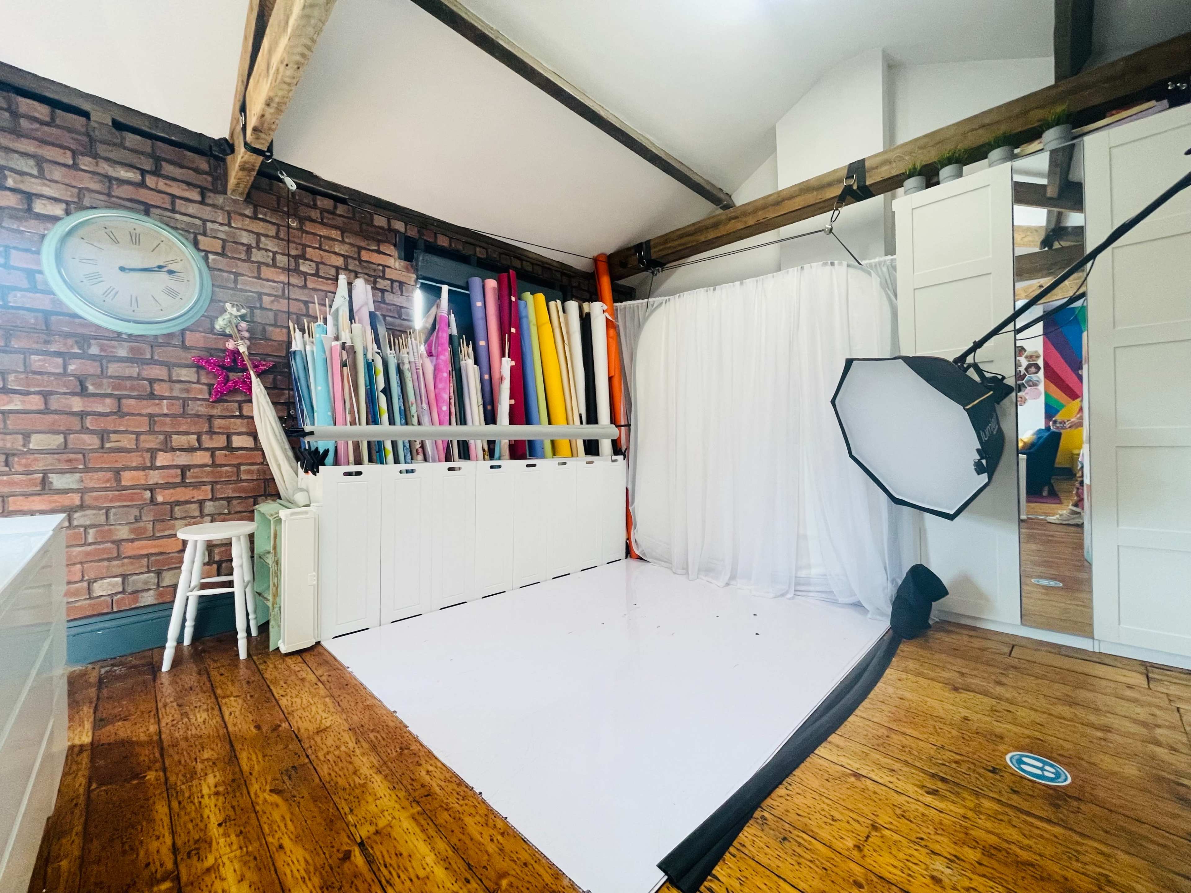 A brightly colored photo studio with a backdrop of colorful paper rolls, a white curtained area, and a softbox lighting setup.