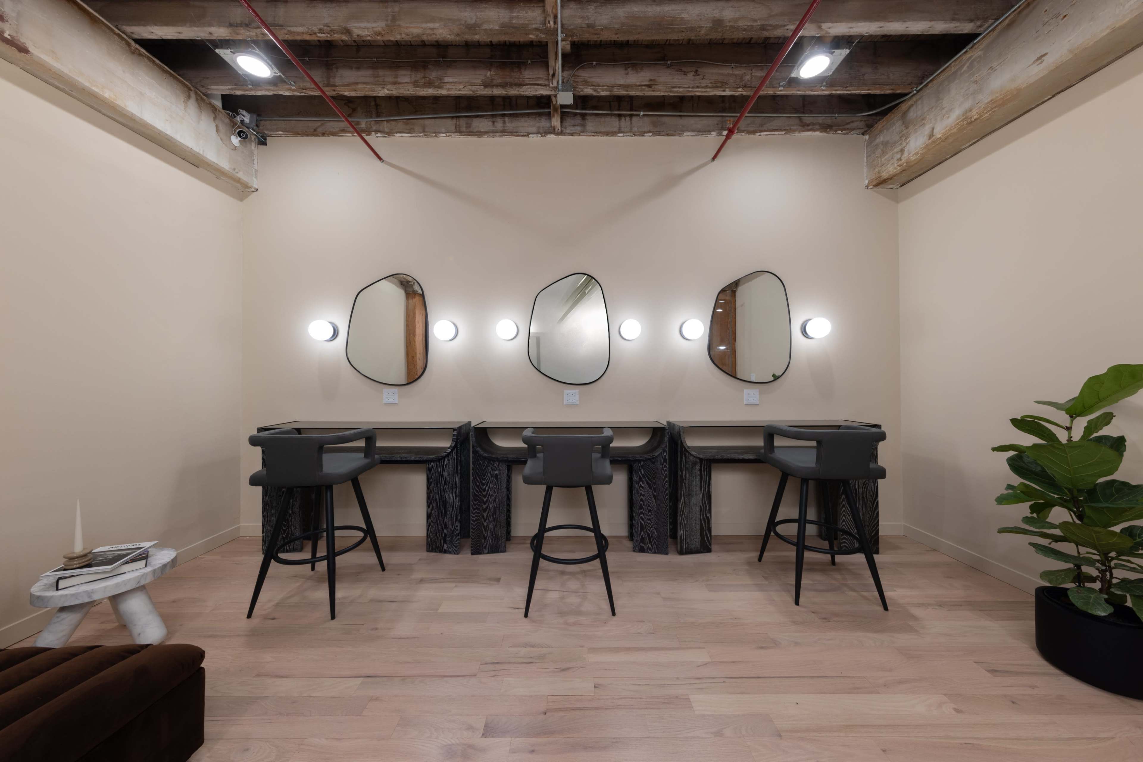 A minimalist interior with three mirrors and matching stools arranged in front of them, complemented by a potted plant in the corner.
