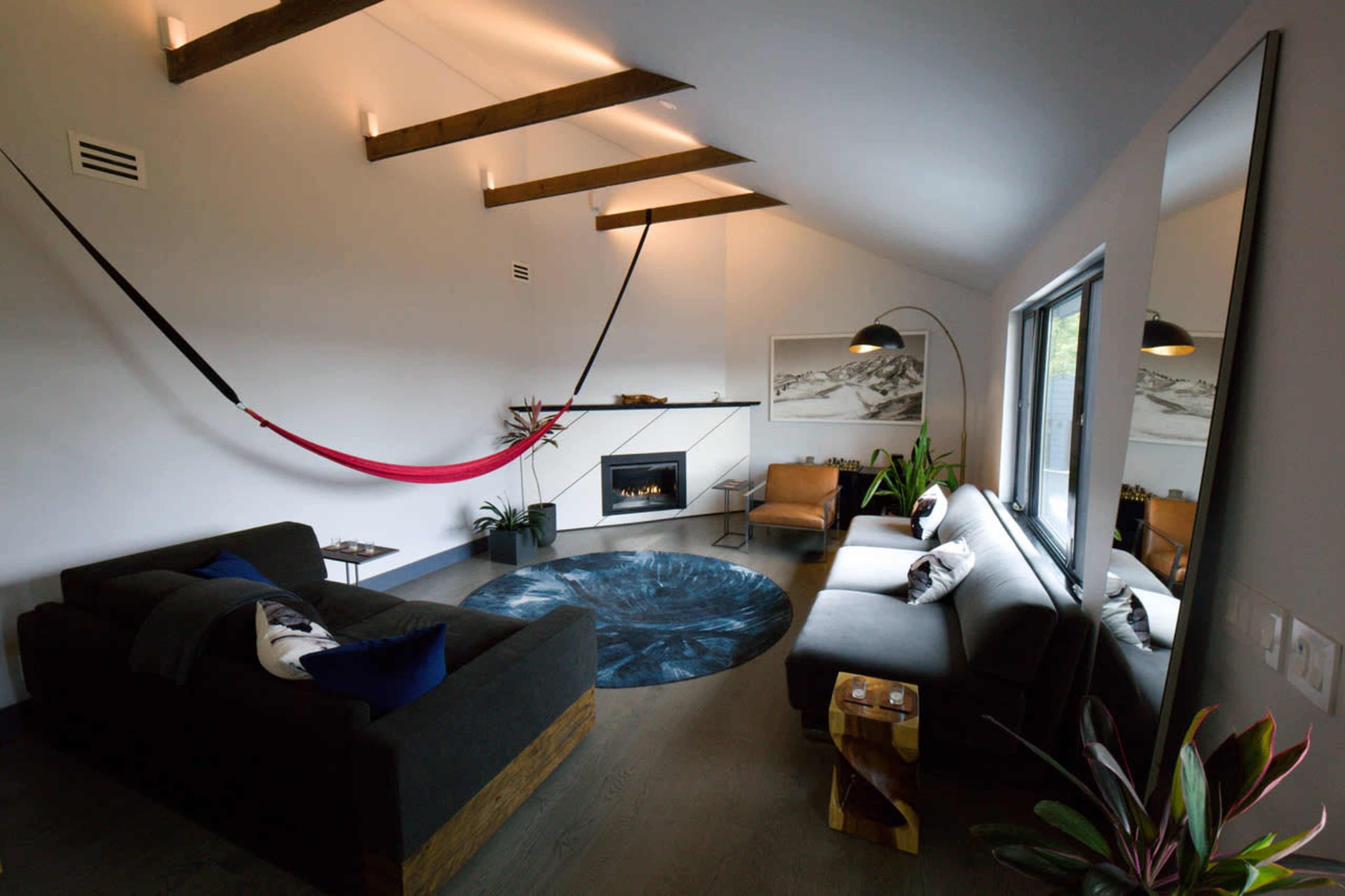 The interior features a modern living space with a hammock suspended from the ceiling, a fireplace, a large rug, and minimalist furniture.