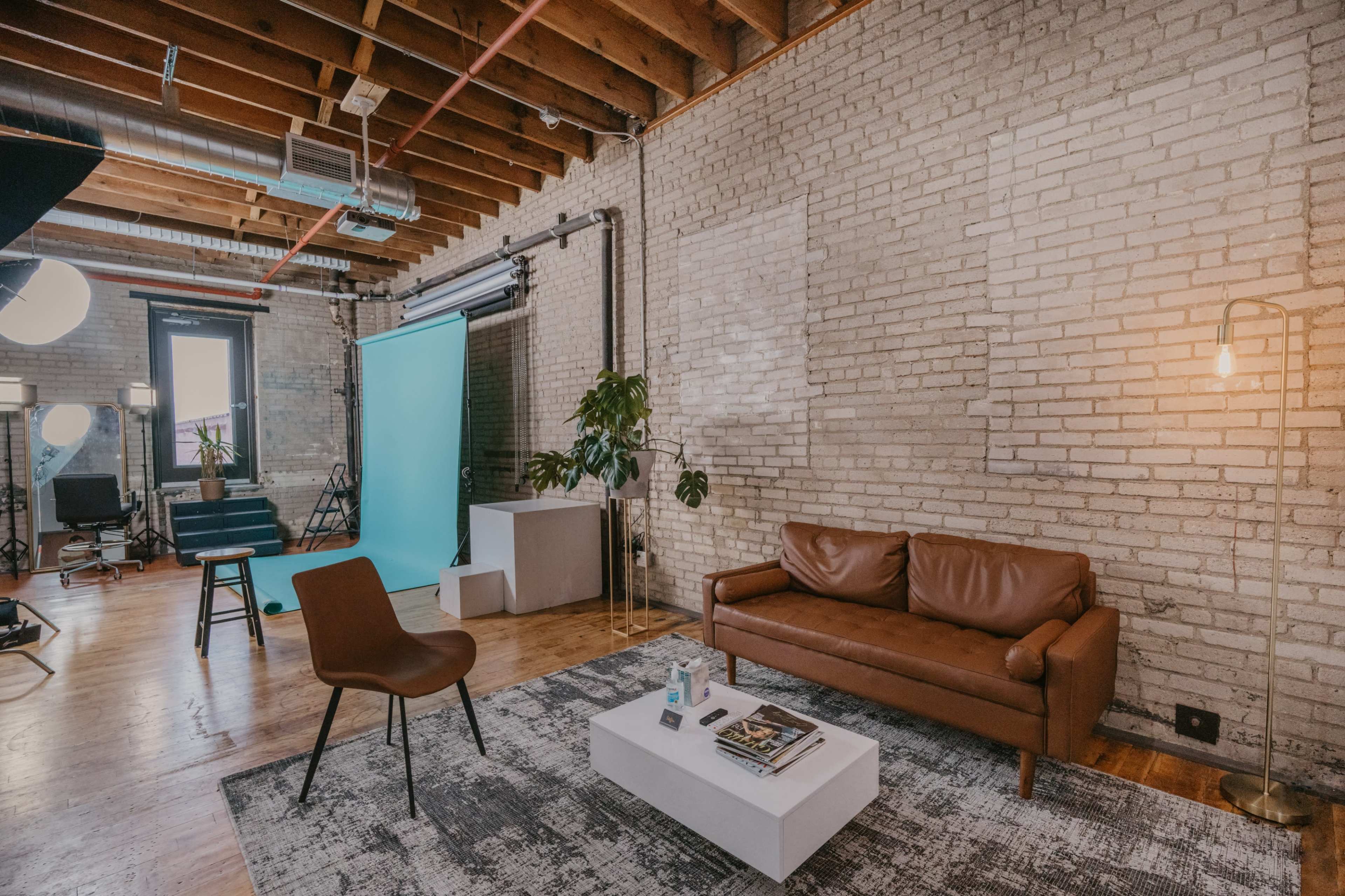 A photography studio with a brown leather sofa, a white coffee table, a backdrop setup, and various lighting equipment.