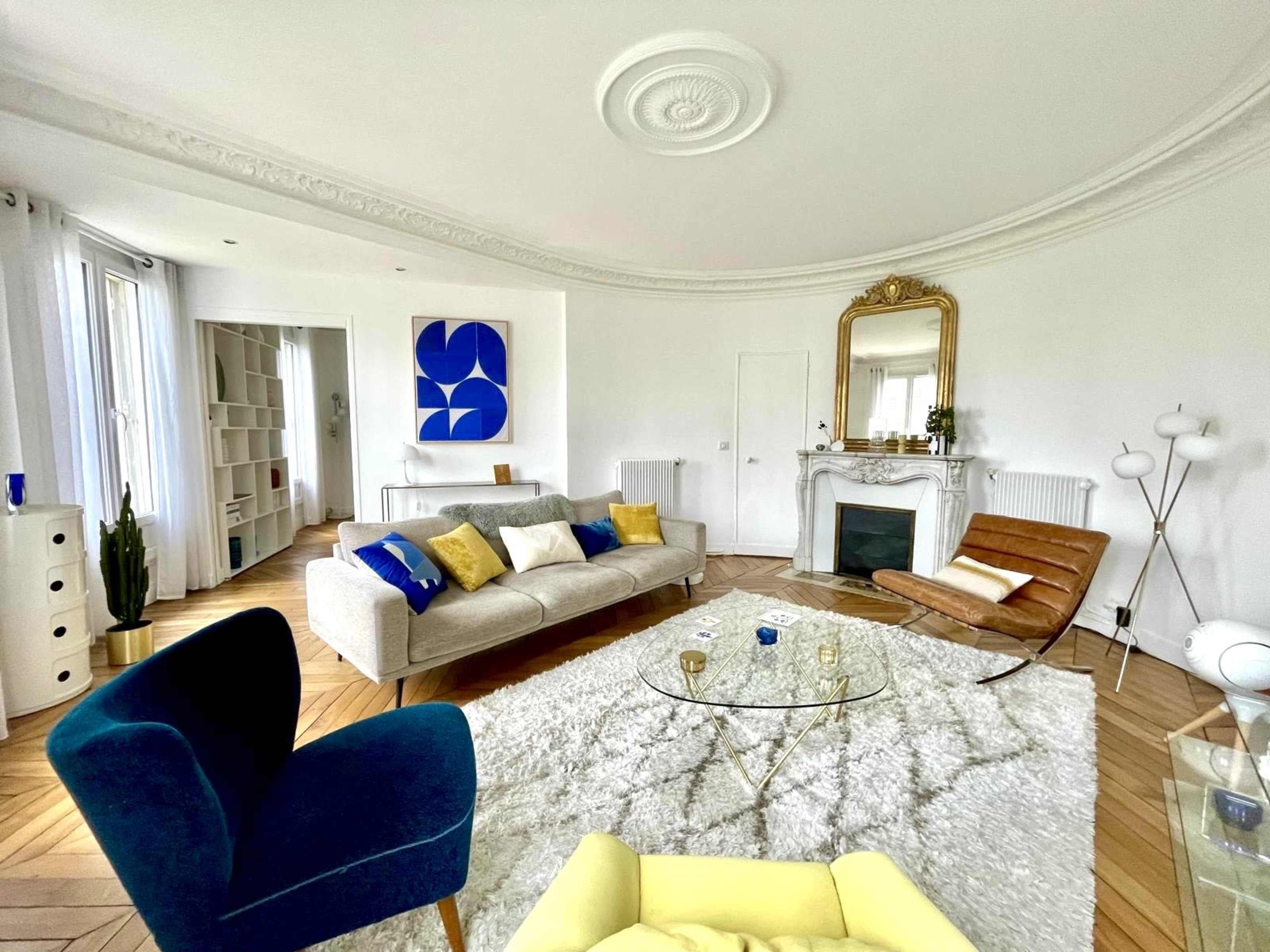 The living room features a stylish arrangement with a sofa, armchairs, a coffee table on a rug, and a decorative fireplace.