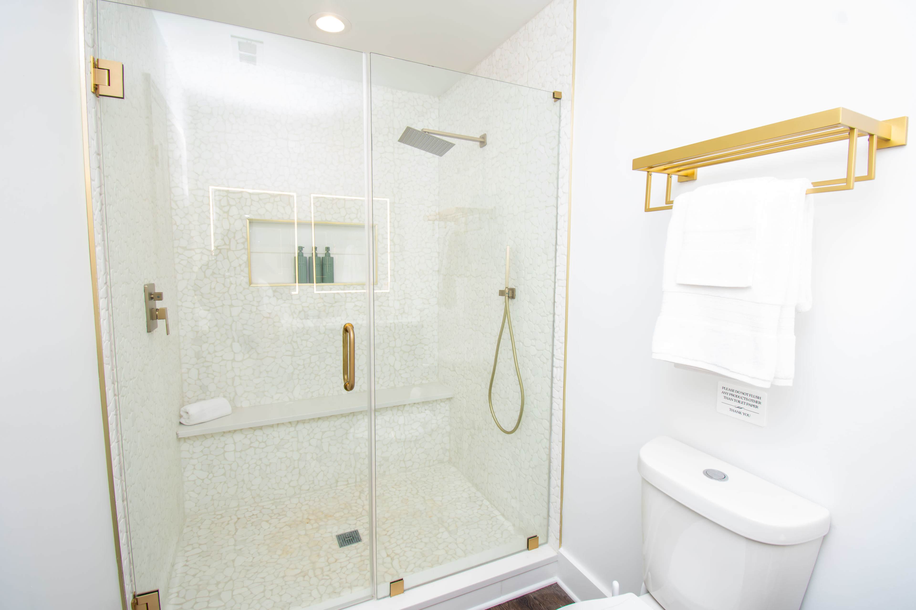 The image features a modern bathroom with a glass-enclosed shower, a toilet, and a towel rack.