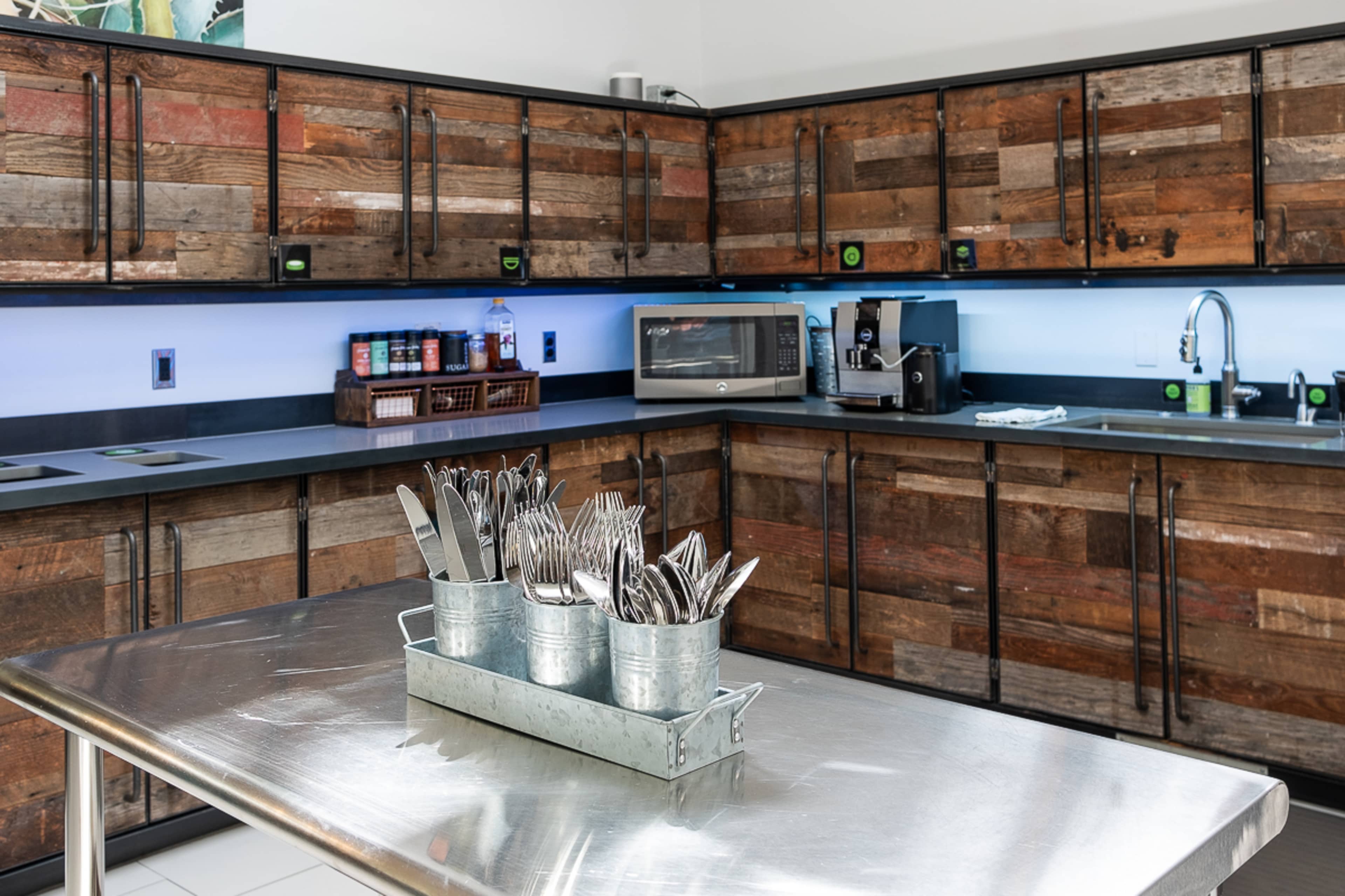 A modern kitchen with wooden cabinets, stainless steel countertops, and utensils displayed in metal containers.
