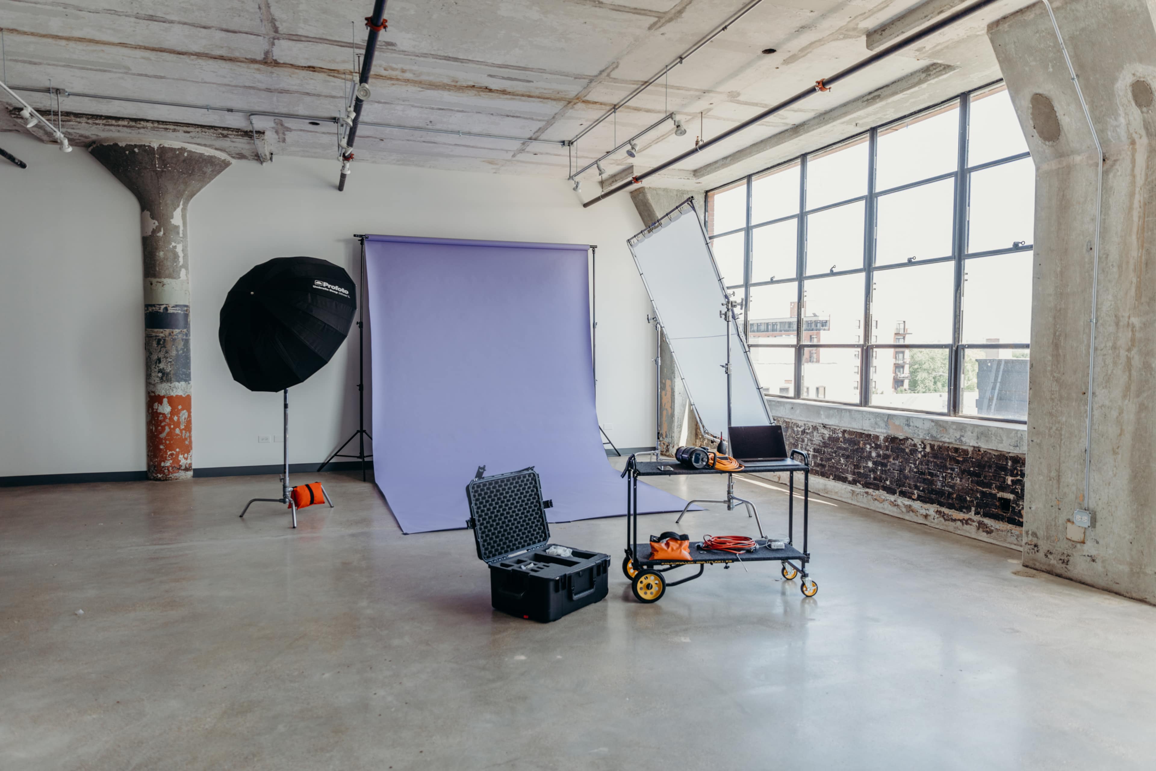 A photography studio with a purple backdrop, lighting equipment, and a cart with tools and accessories in an industrial-style space.