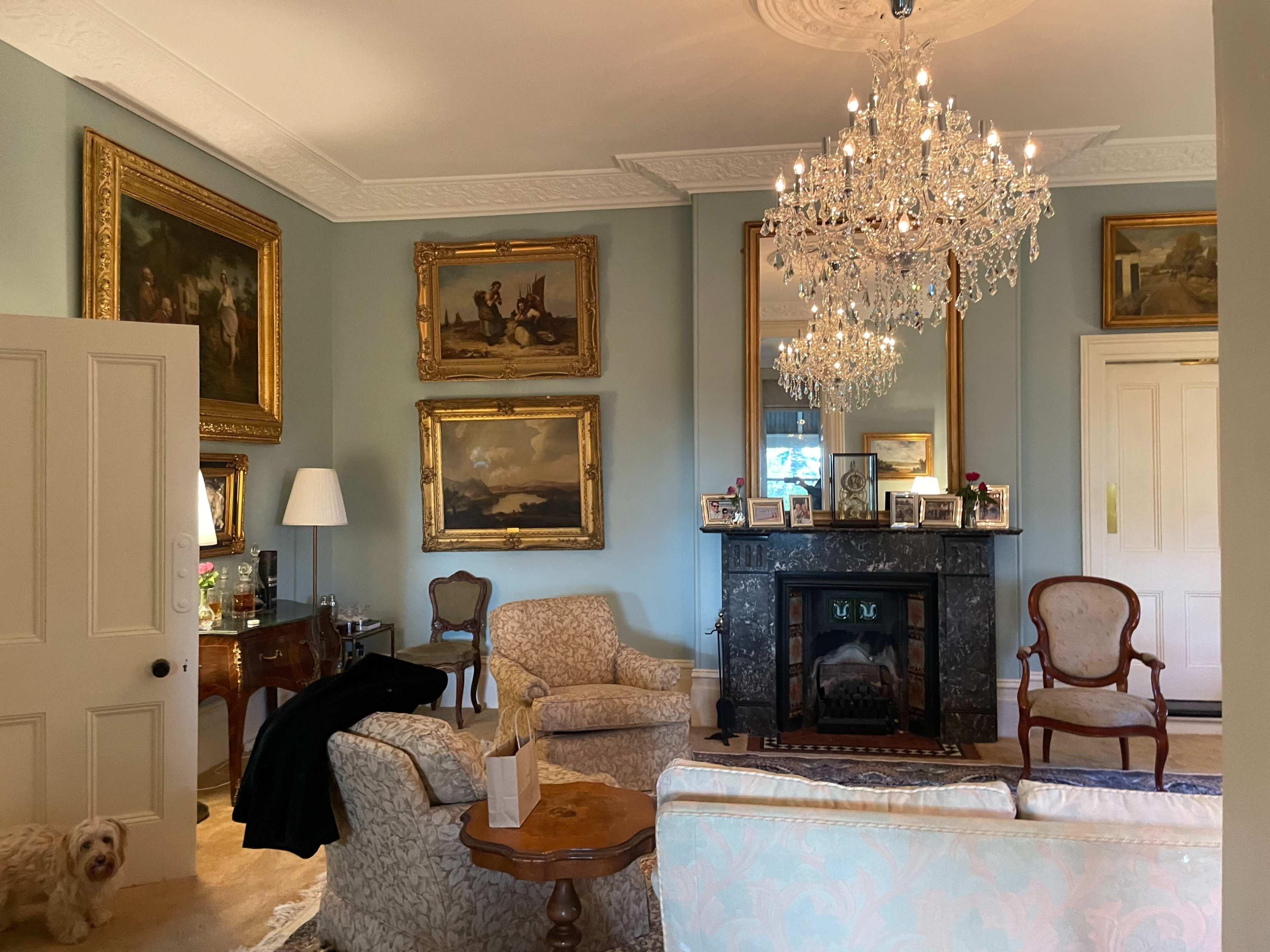 A well-decorated living room featuring a chandelier, vintage paintings in ornate frames, and a fireplace.
