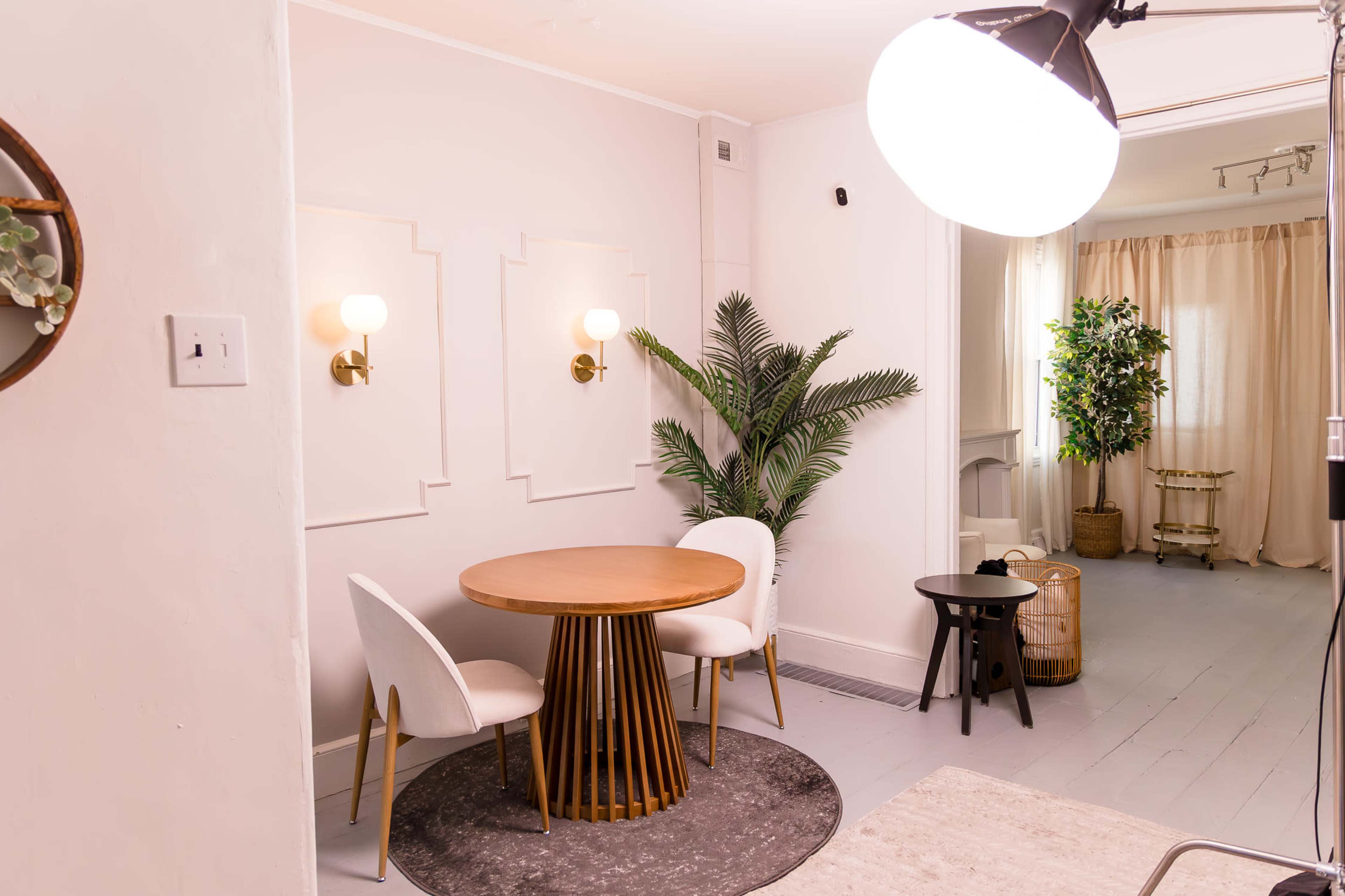 The image shows a cozy dining area featuring a round wooden table with two upholstered chairs, a decorative plant, and soft lighting.
