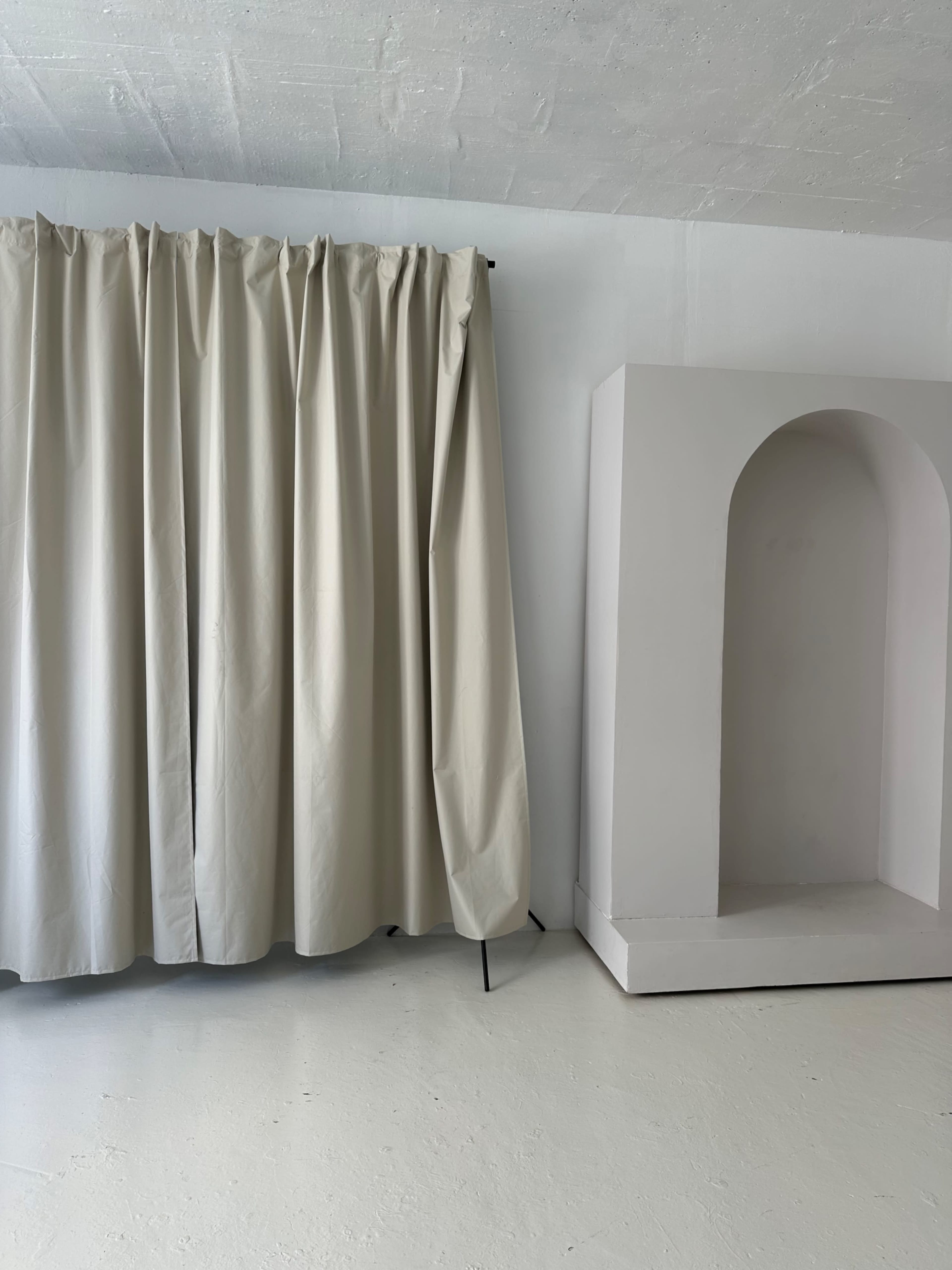 The image shows a light beige curtain hanging on a metal rod next to a white archway niche built into the wall.