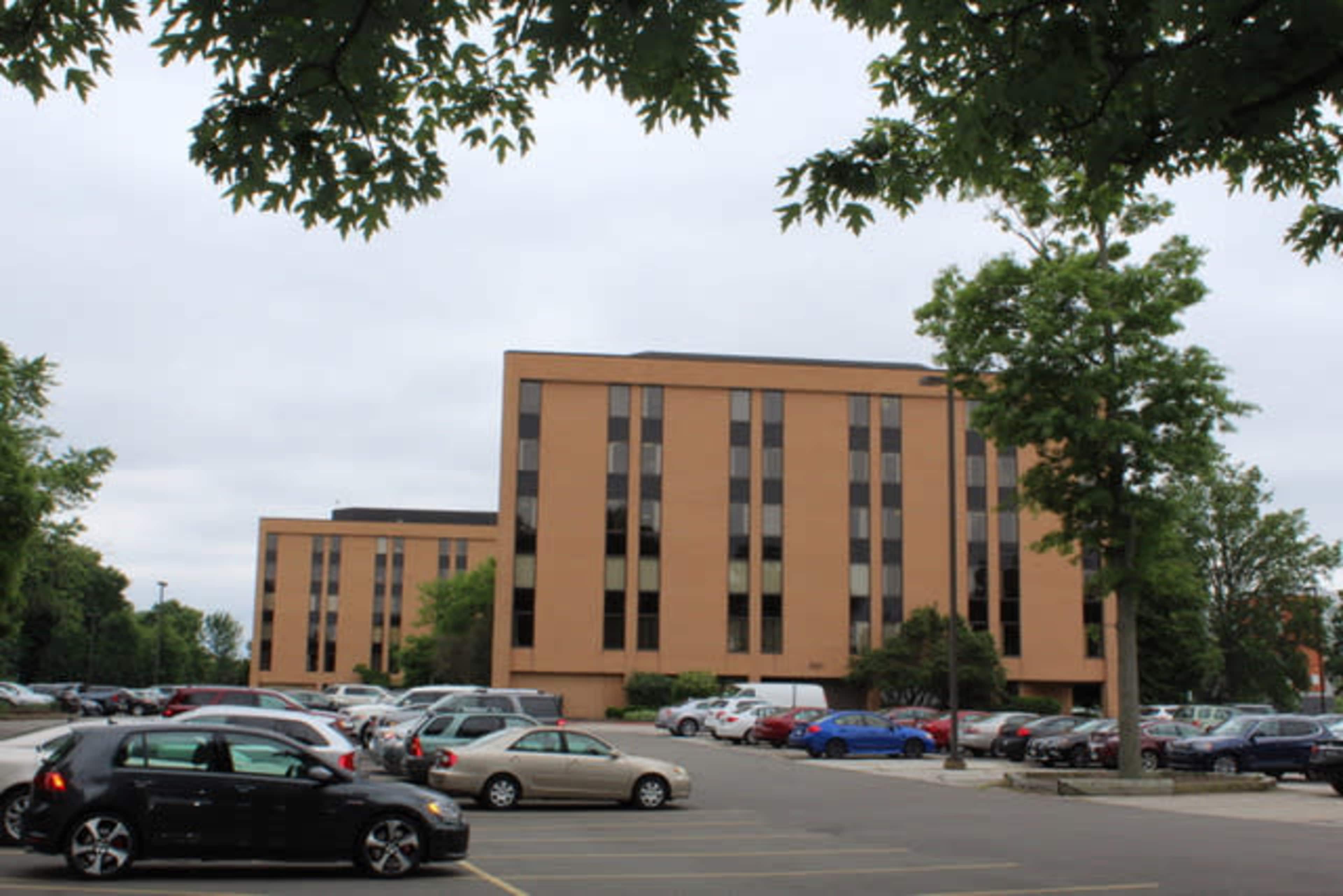 A multi-story brown building surrounded by a parking lot filled with various parked cars.